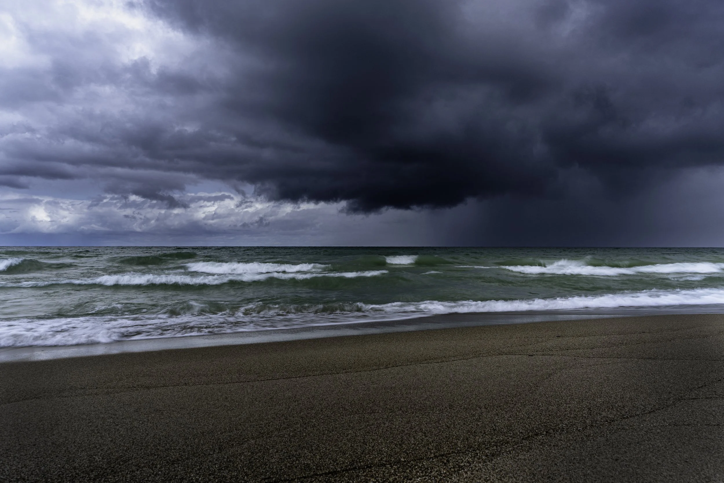 A stormy sky with dark clouds over a beach, with waves crashing onto the sand.