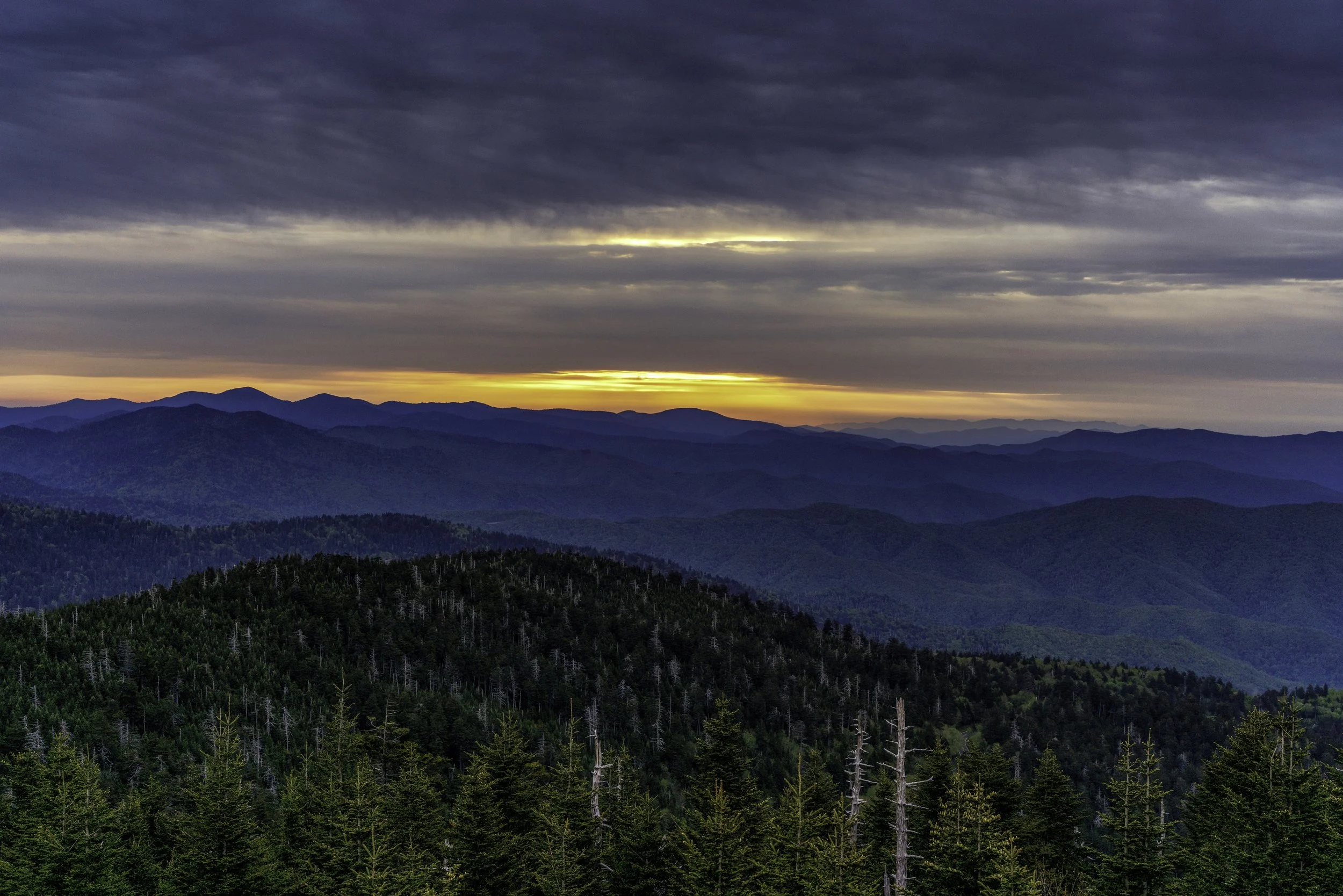 A scenic view of a mountainous landscape during sunset, with layered mountain ranges and a partly cloudy sky.