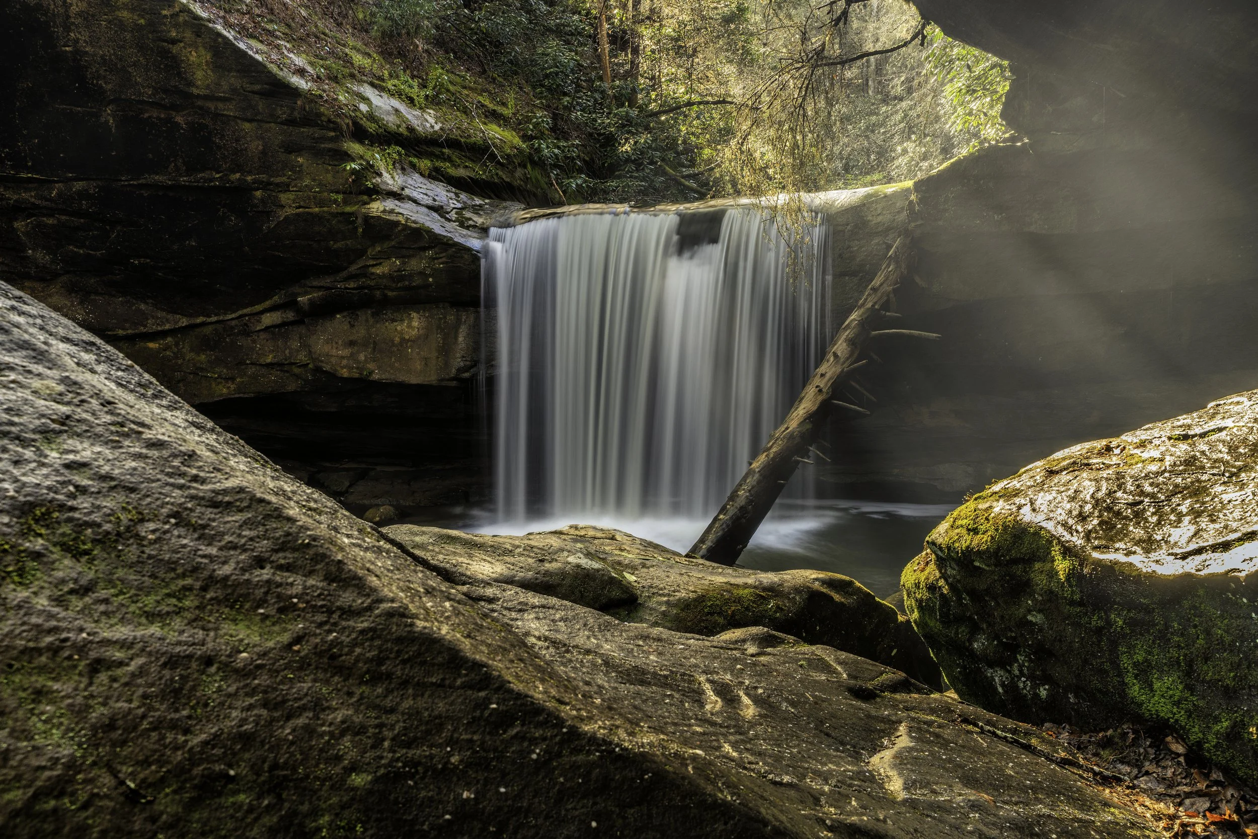 A small waterfall flowing over rocks in a forest with sunlight filtering through trees.