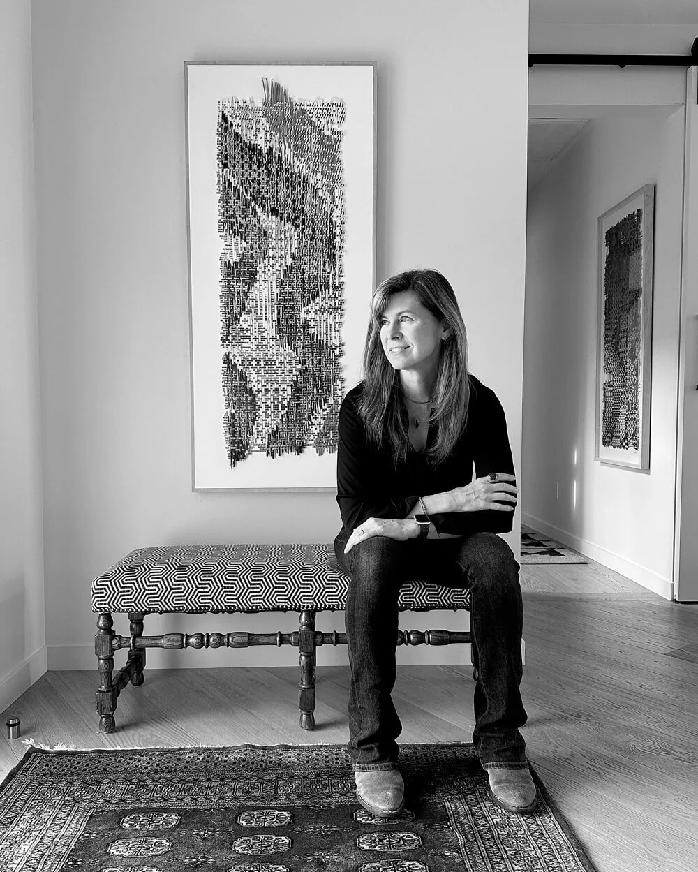 Weaver and artist Libby Raab seated beside one of her woven artworks in her studio.