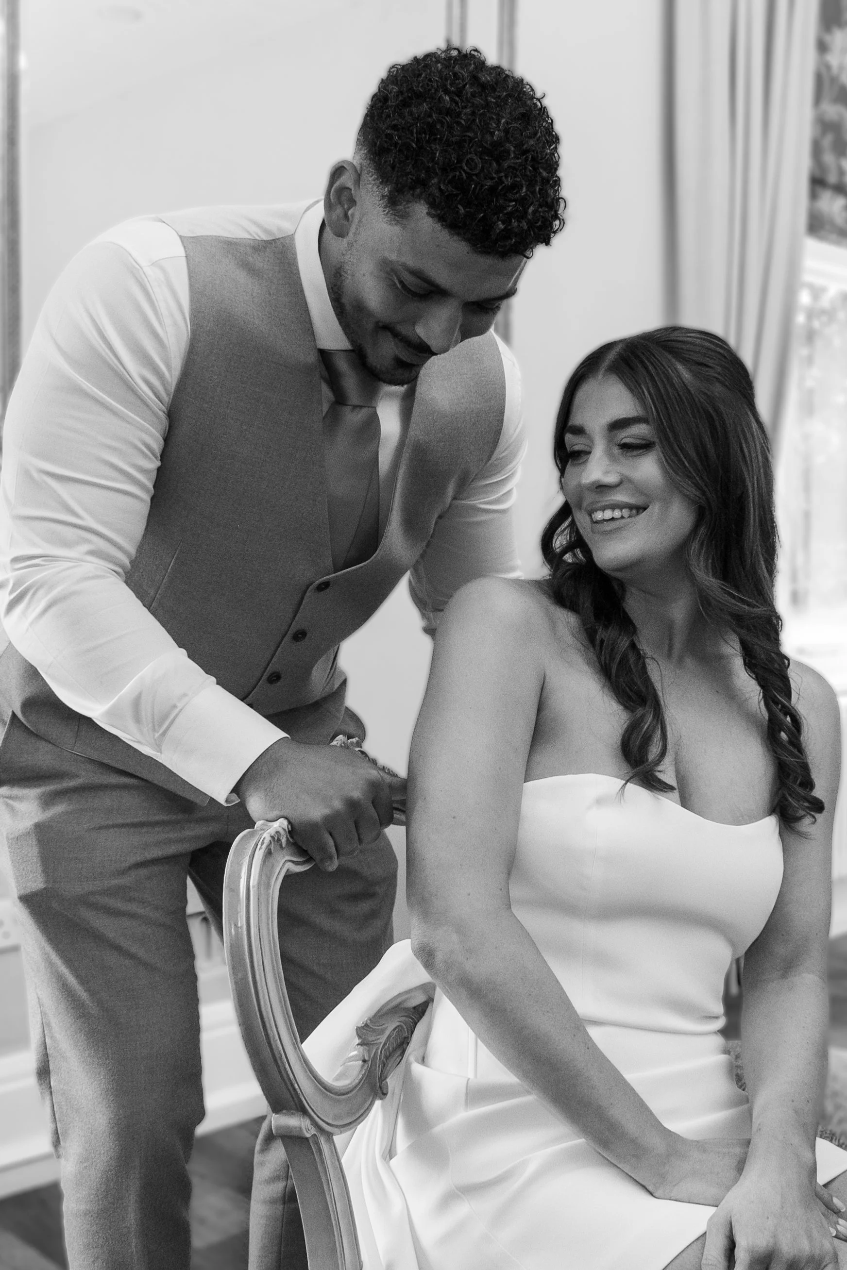A groom in a vest and tie gently holds the arm of the bride in a strapless dress, both smiling, in West Bridgeford Registry Office.