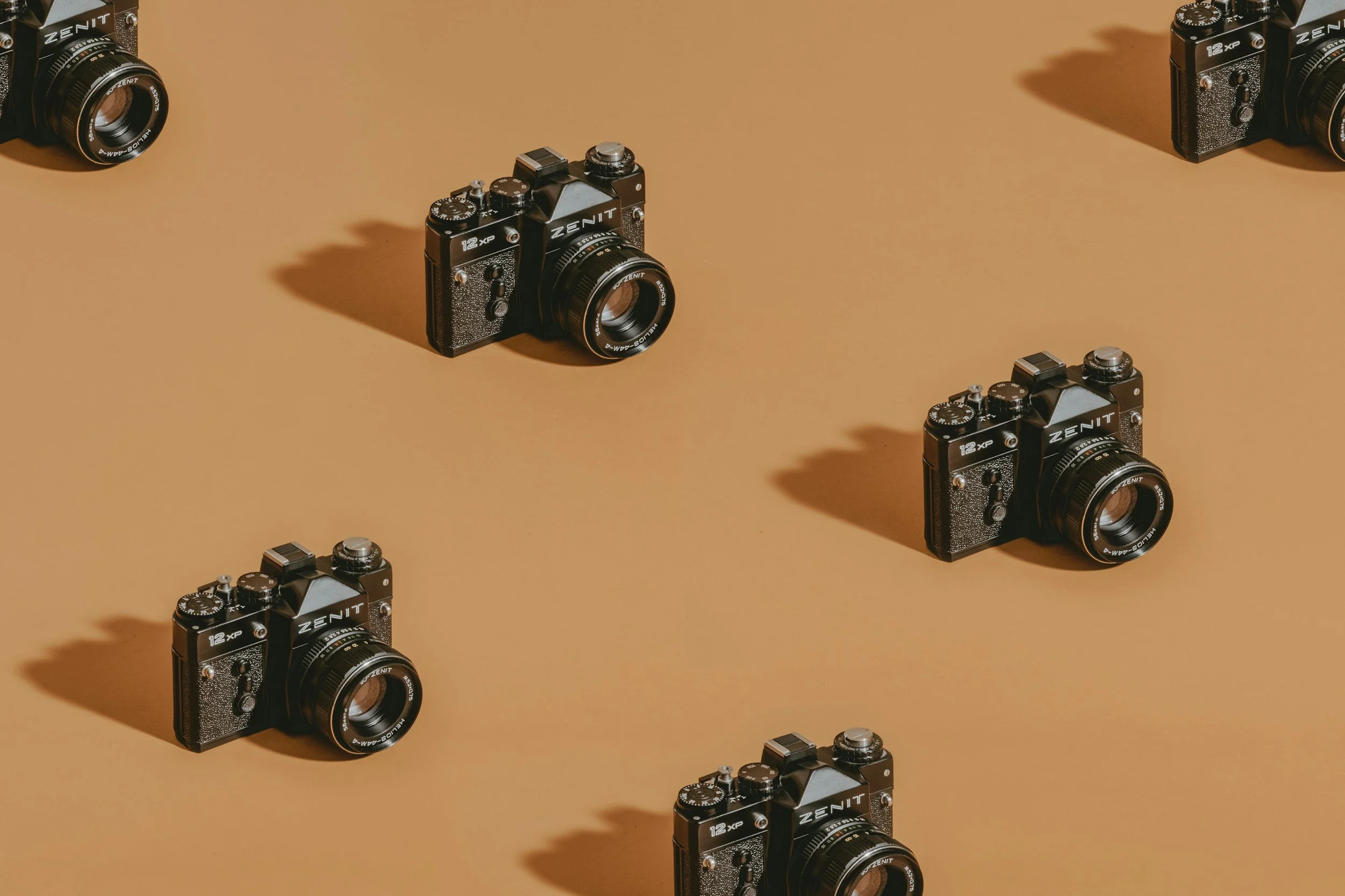 Multiple vintage black cameras with silver accents and labeled 'ZENIT' arranged on a beige surface, casting shadows.