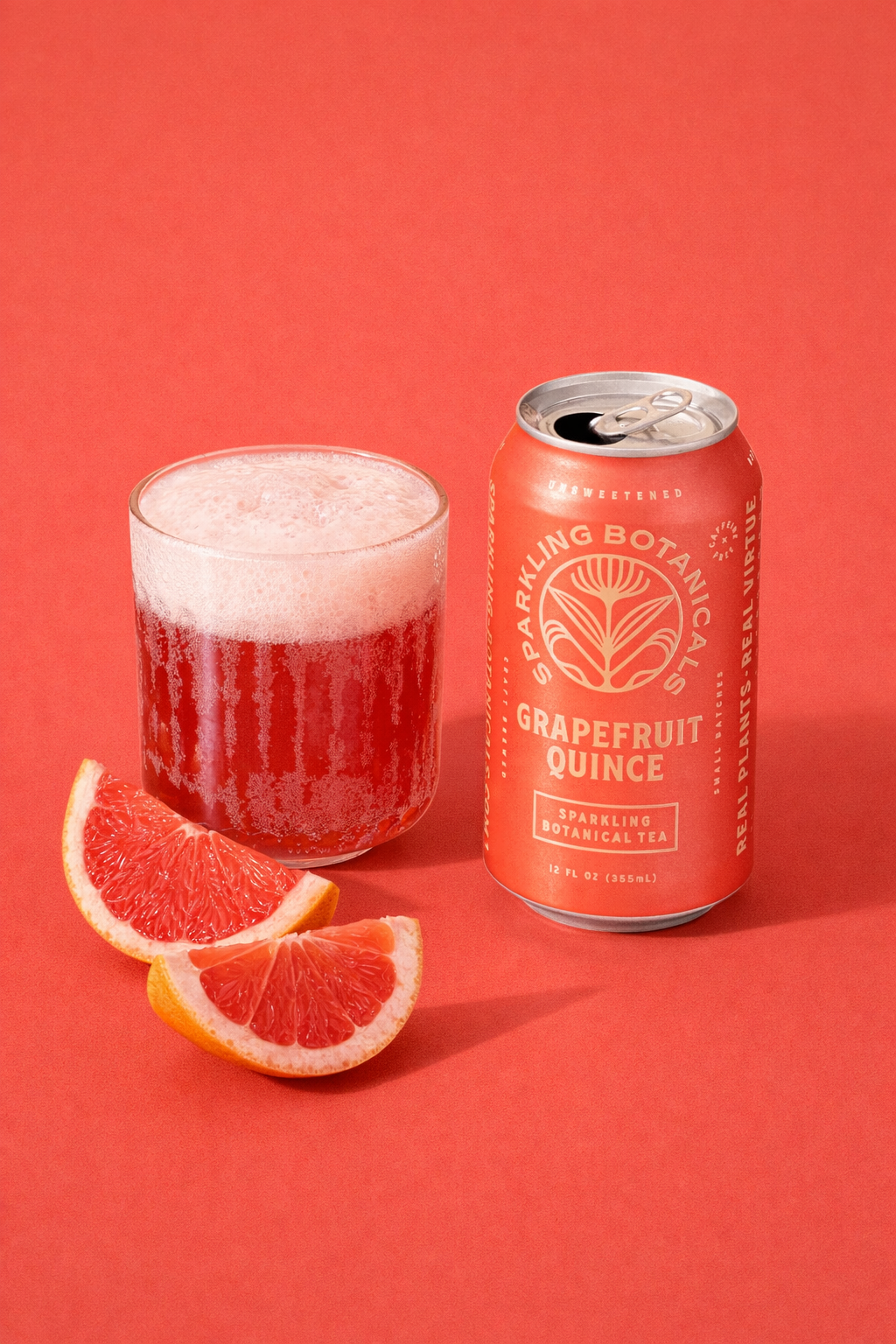 A can of Sparkling Botanical Tea Grapefruit Quince next to a glass filled with the beverage and three slices of grapefruit on a coral background.