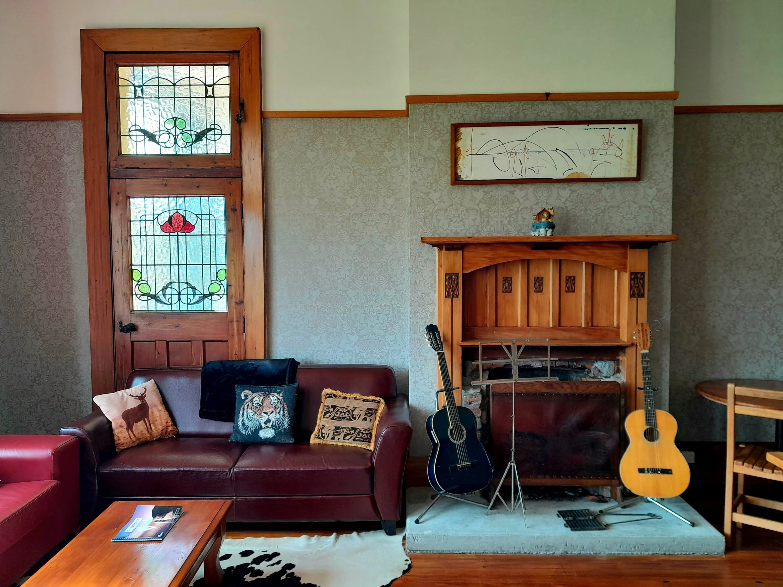 Lounge area in dining room with leather sofas, cowhides, and guitars at heritage flashpacker accommodation in Greymouth, West Coast, New Zealand.