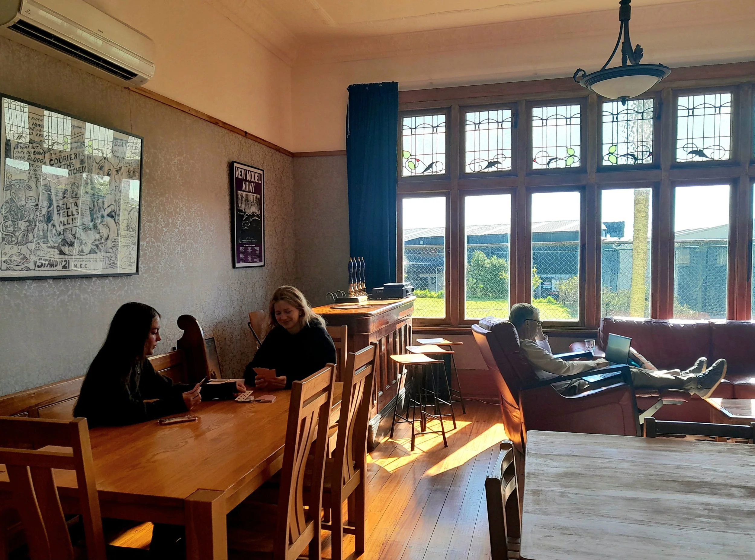 A warm, inviting dining room at Noah's Ark Fleshpacker filled with natural light, where people gather around table to share laughter, and conversation or relax in cozy leather reclining armchair and sofas.
