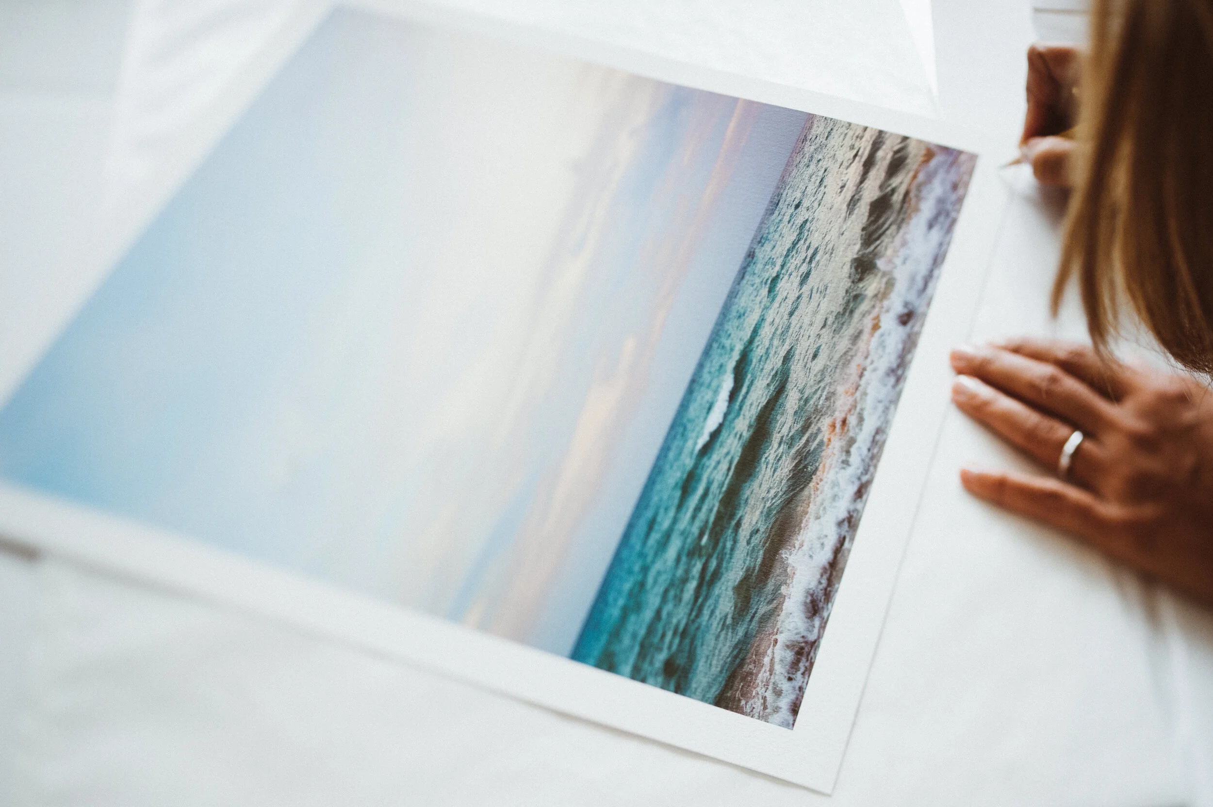 Person looking at a photograph of the ocean on a white table.