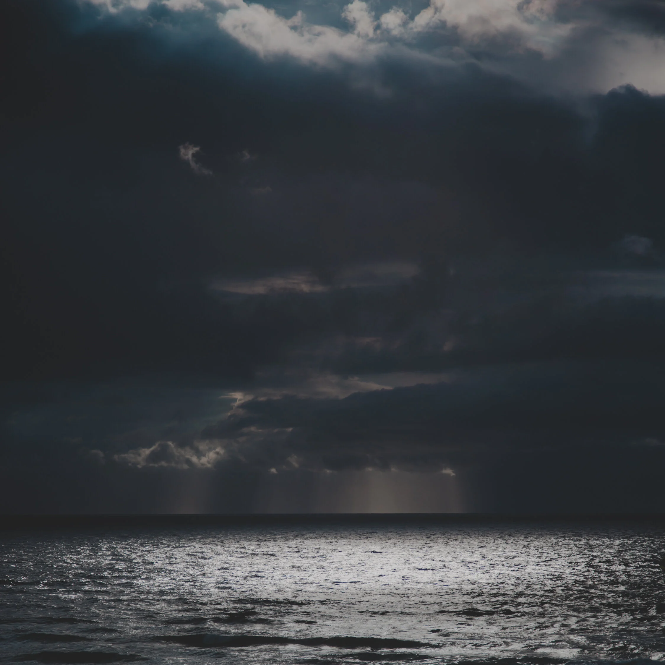 Dark storm clouds over a rough ocean, with faint rays of sunlight breaking through