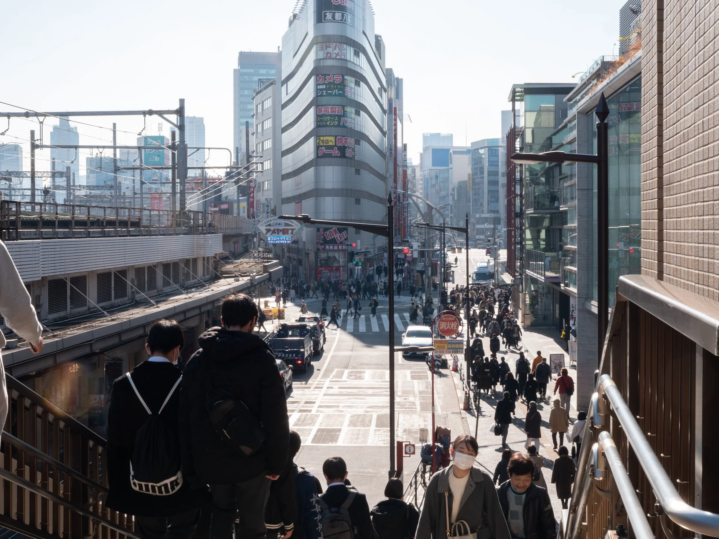 Urban street scene with crowds of pedestrians crossing the street, tall buildings with colorful signs, and people walking in an Asian city, likely Tokyo, Japan.