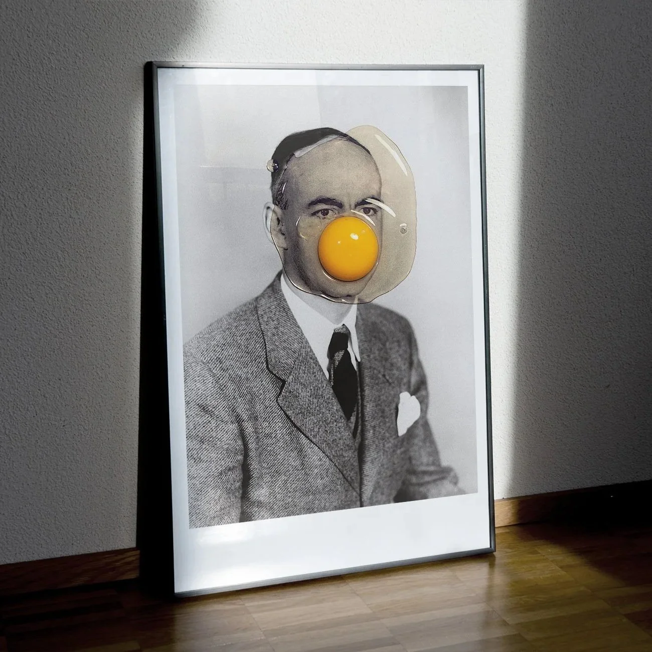 Photographie en noir et blanc d'un homme portant un costume, avec un œuf frit orange placé sur son visage en guise de nez, créant une œuvre artistique.
