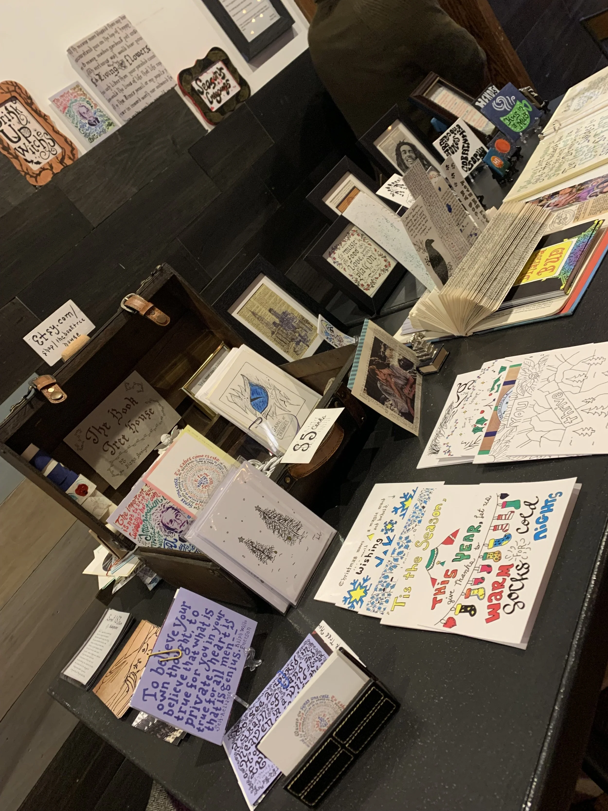 Sanger Hall Holiday Art Faire table featuring cards, calligraphy, bookmarks and upcycled book pages, Sunnyside Queens. December 2021