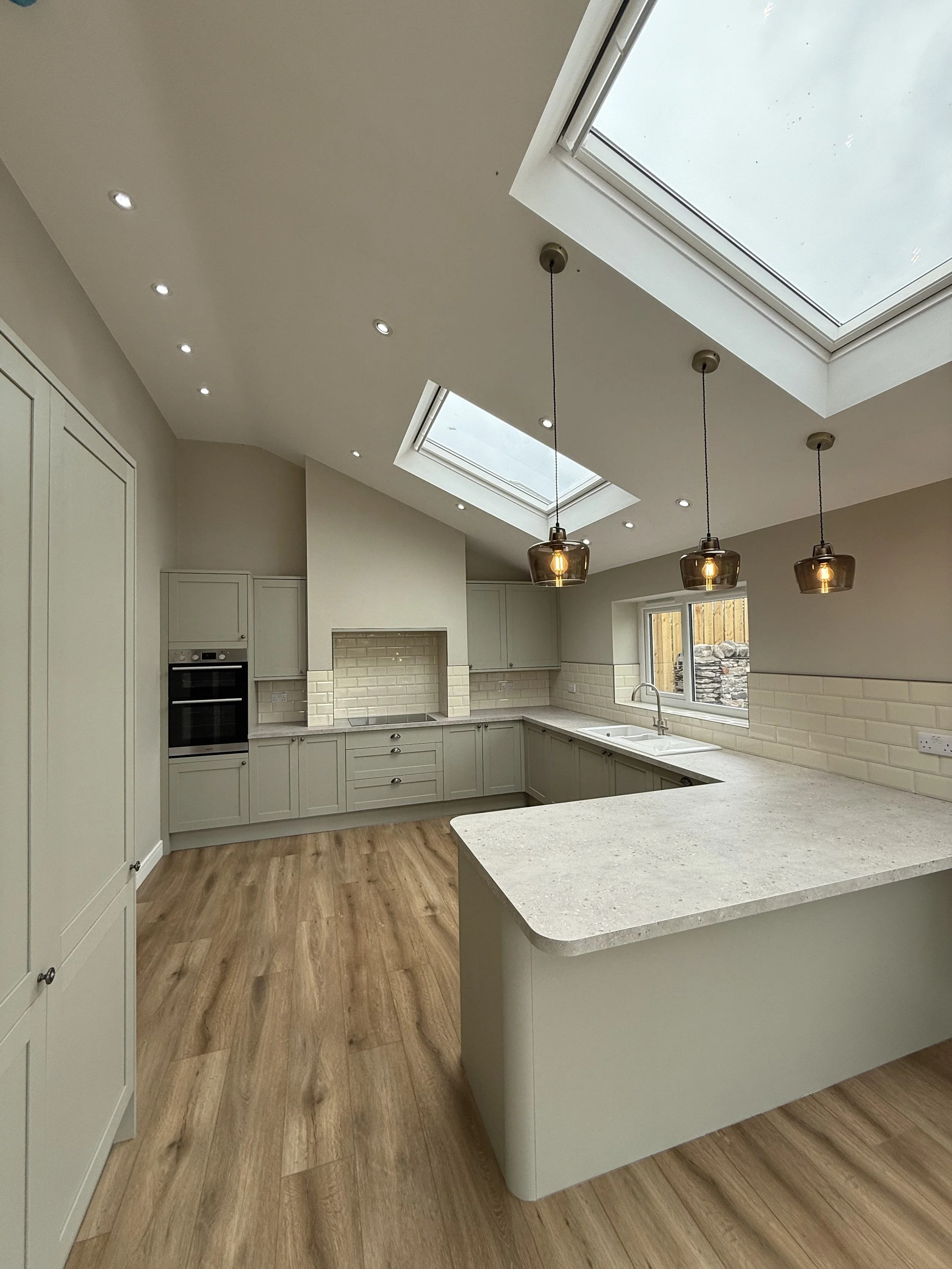 Modern kitchen with cream-colored cabinets, wooden flooring, a large countertop, under-cabinet lighting, and two skylights.