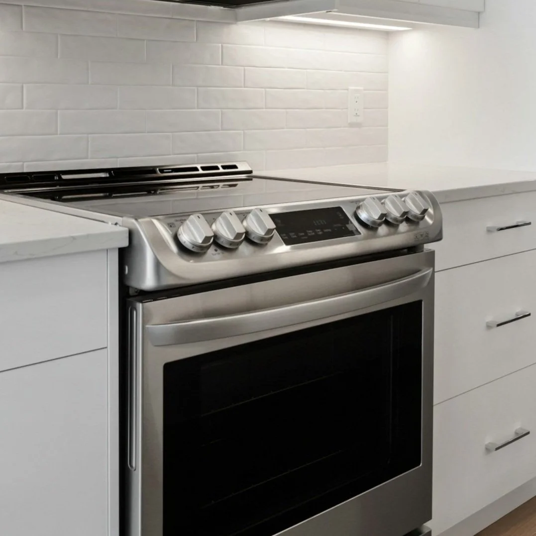 Stainless steel electric stove with four burners and a digital control panel, situated in a modern kitchen with white cabinetry and a white brick backsplash.