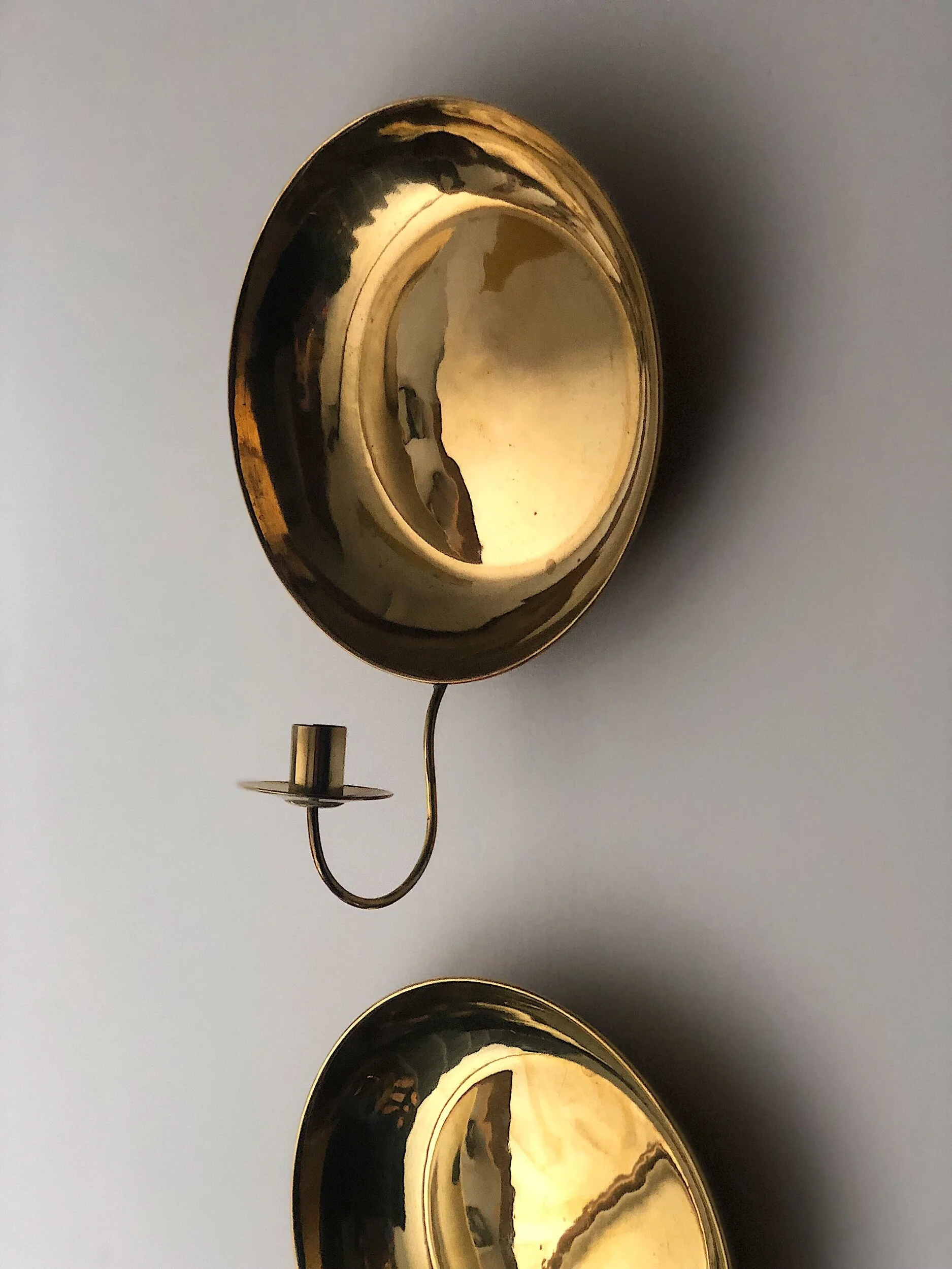 Two brass wall-mounted candle holders with a reflective finish.