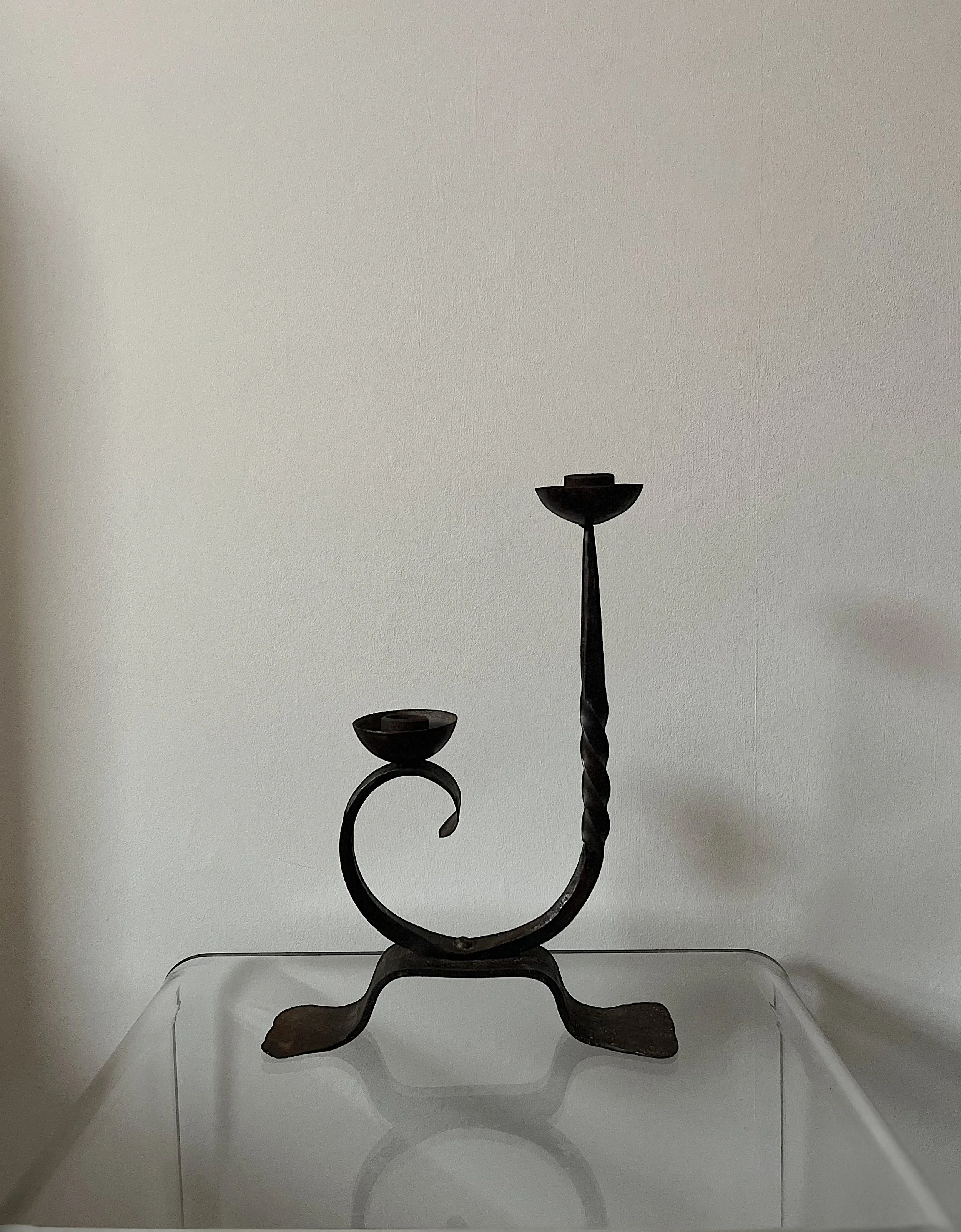 Wrought iron candle holder with two holders, twisted and curved design, on glass table.