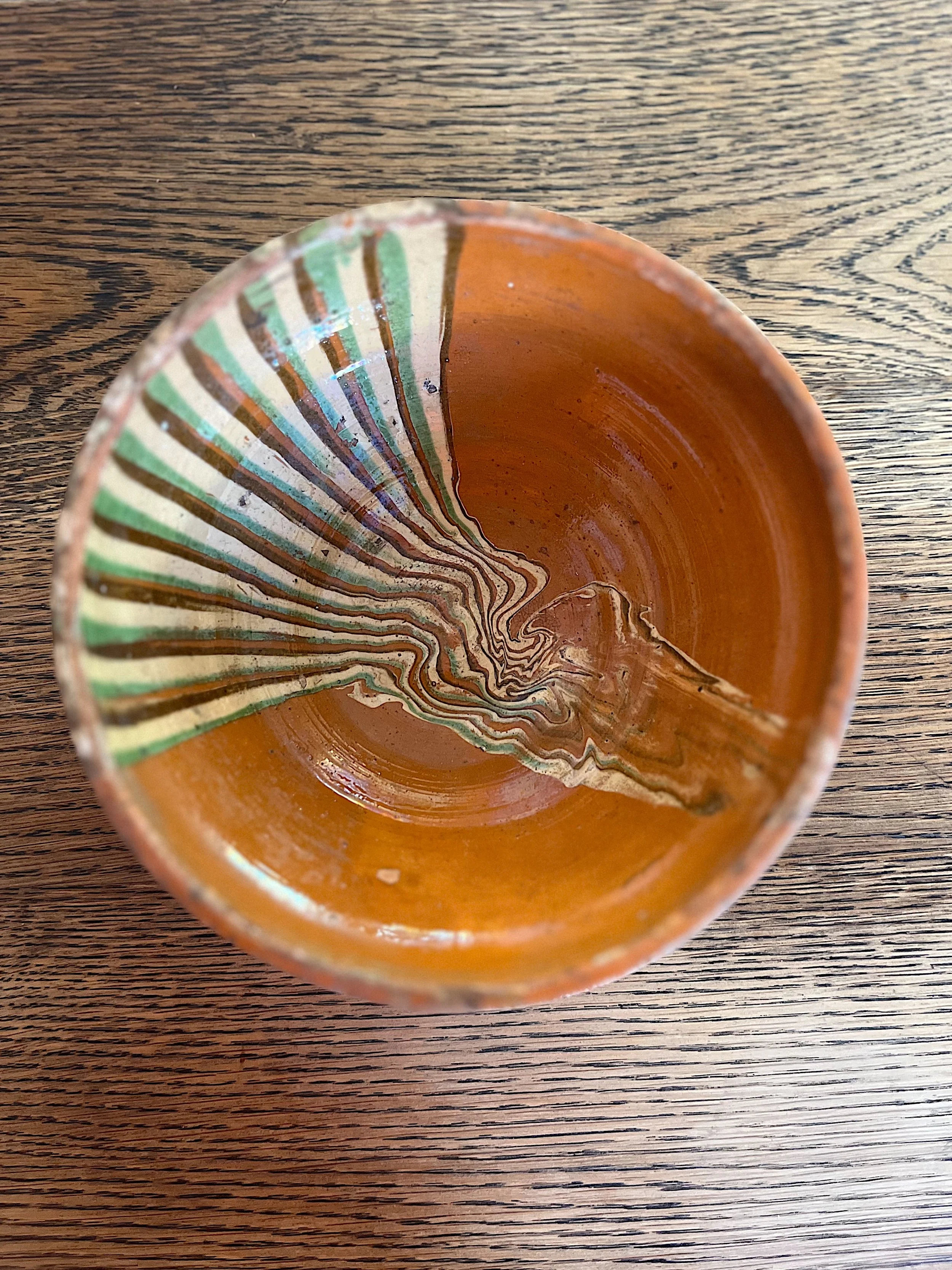Top view of a ceramic bowl on a wooden table, featuring a unique pattern of wavy brown and green lines inside.