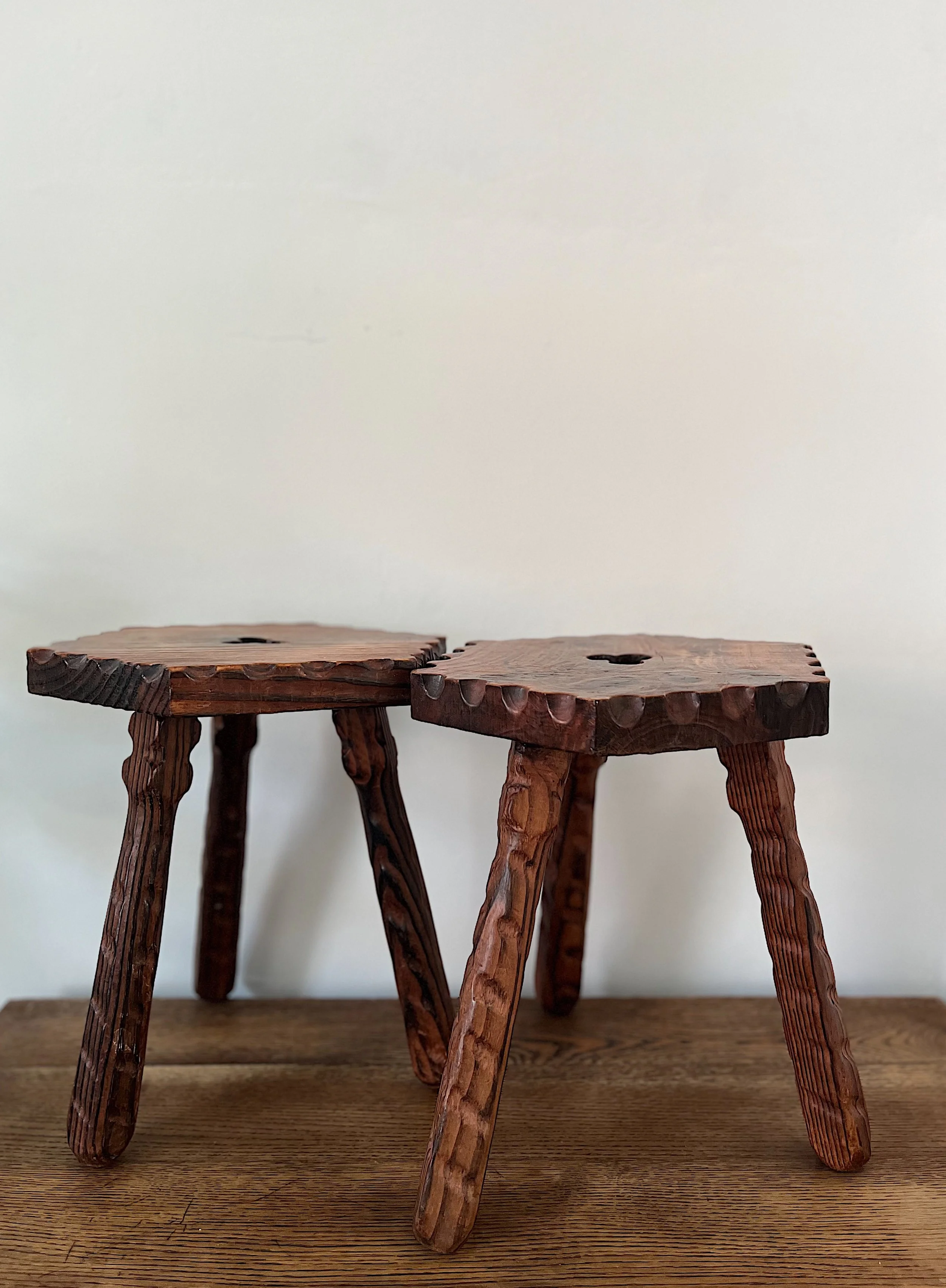 Two rustic wooden stools with carved legs and textured round seats placed on a wooden surface.
