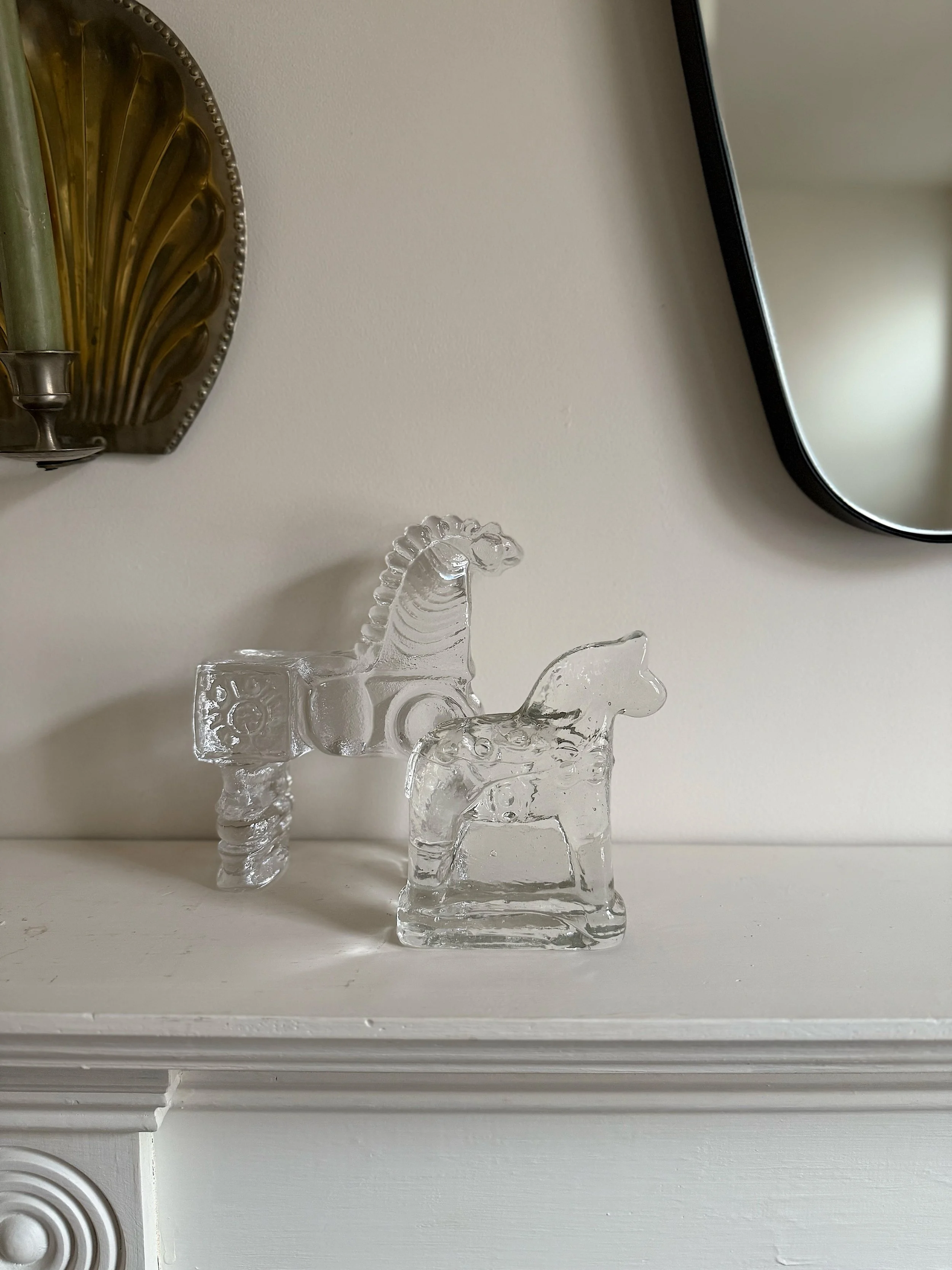 Glass horse figurines on white shelf with mirror and brass candlestick