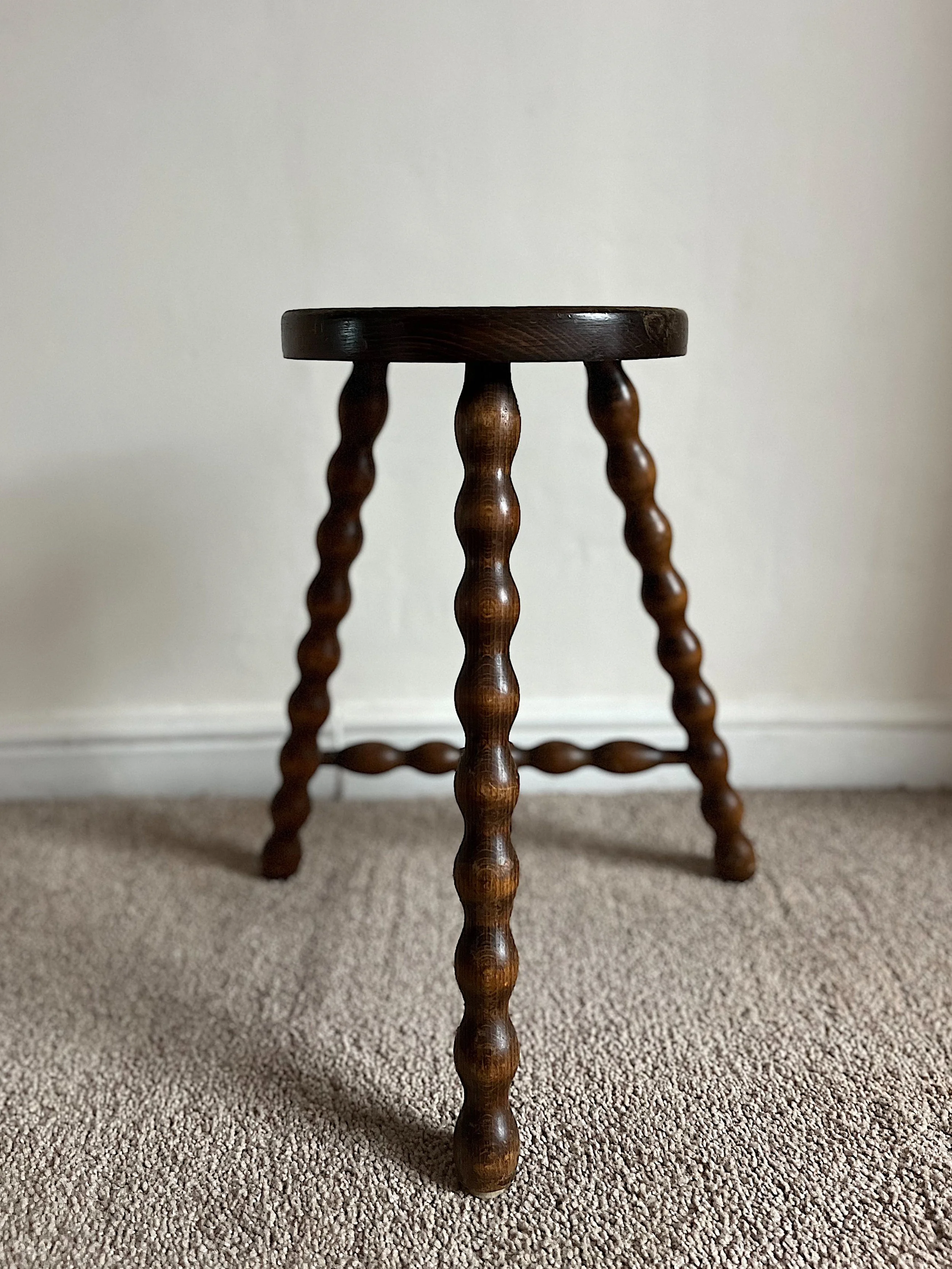 Wooden stool with spiral legs on carpeted floor against a white wall.
