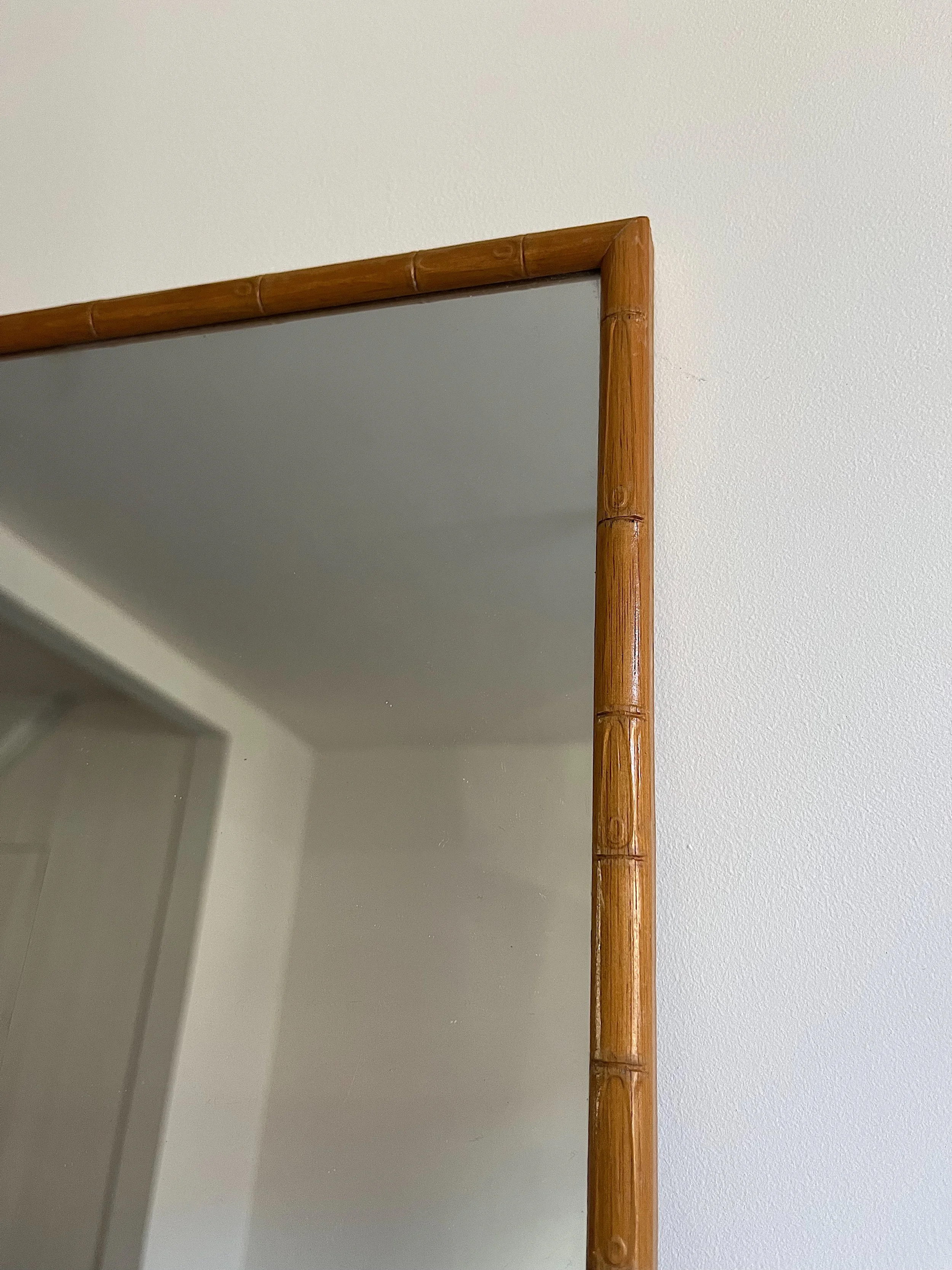 Close-up of a mirror with a bamboo-style frame against a white wall.