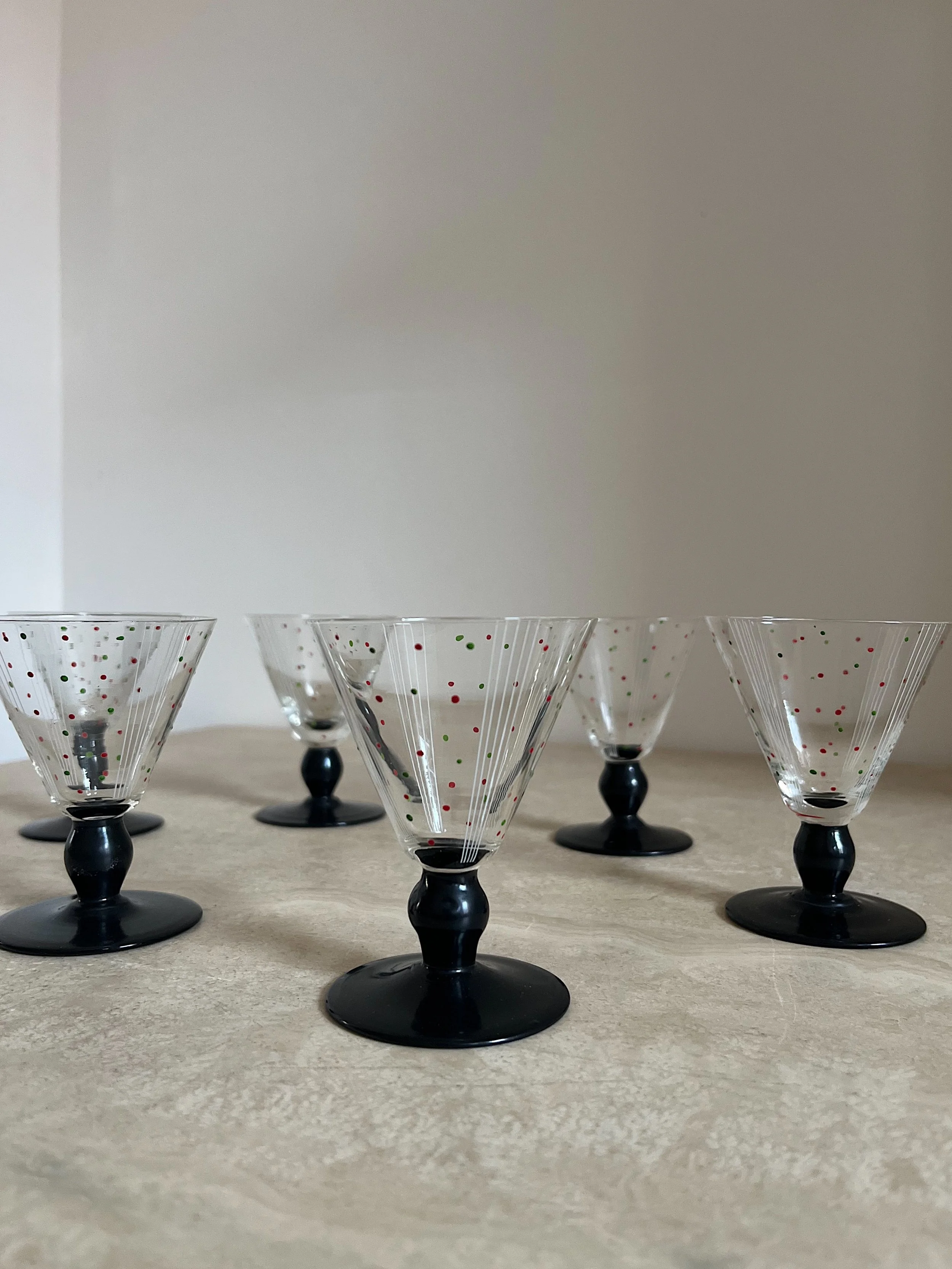 Set of six vintage cocktail glasses with black stems and patterned designs on a light surface.