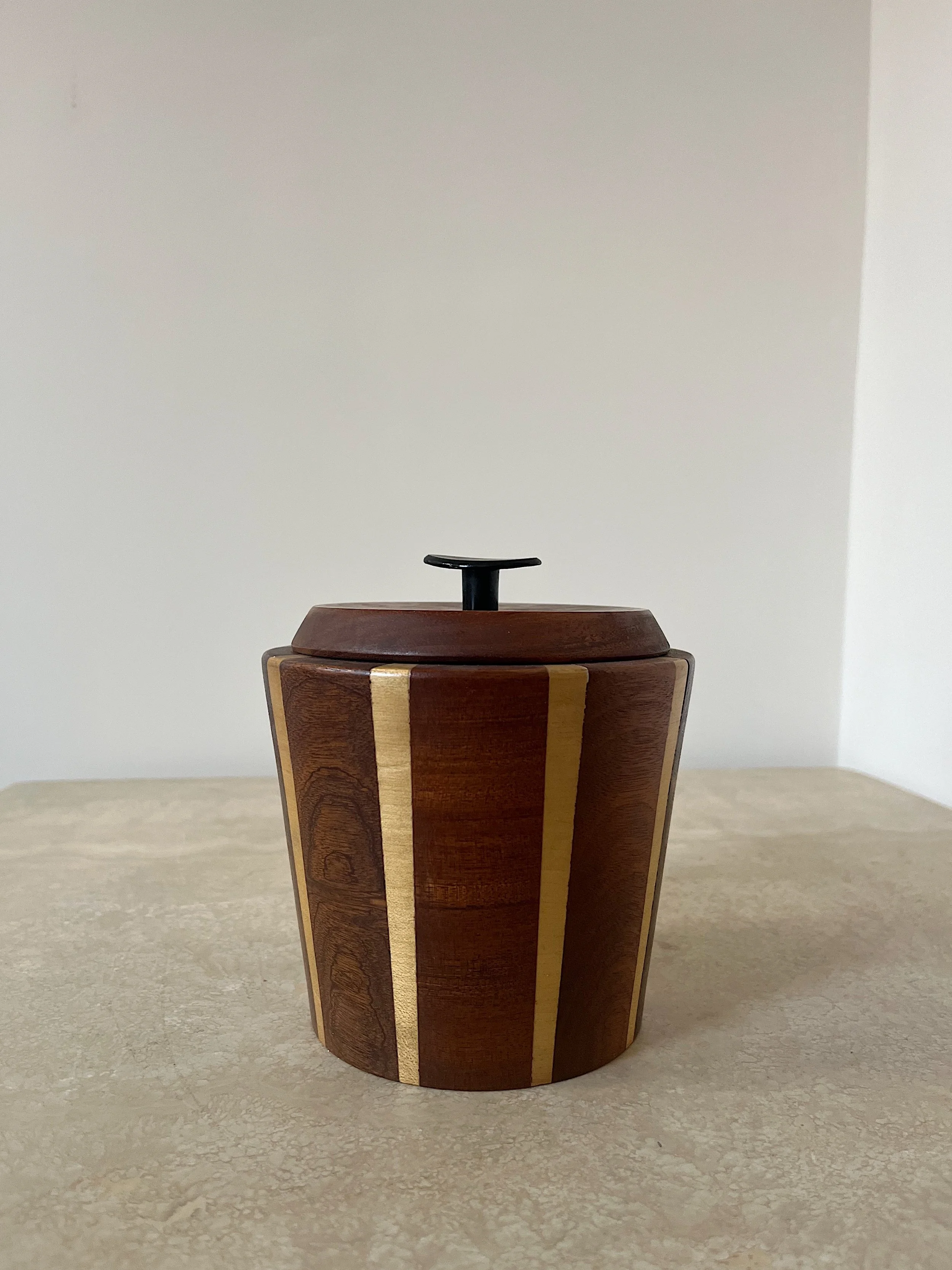 Wooden container with a lid and black knob, featuring decorative vertical lines on a beige surface.