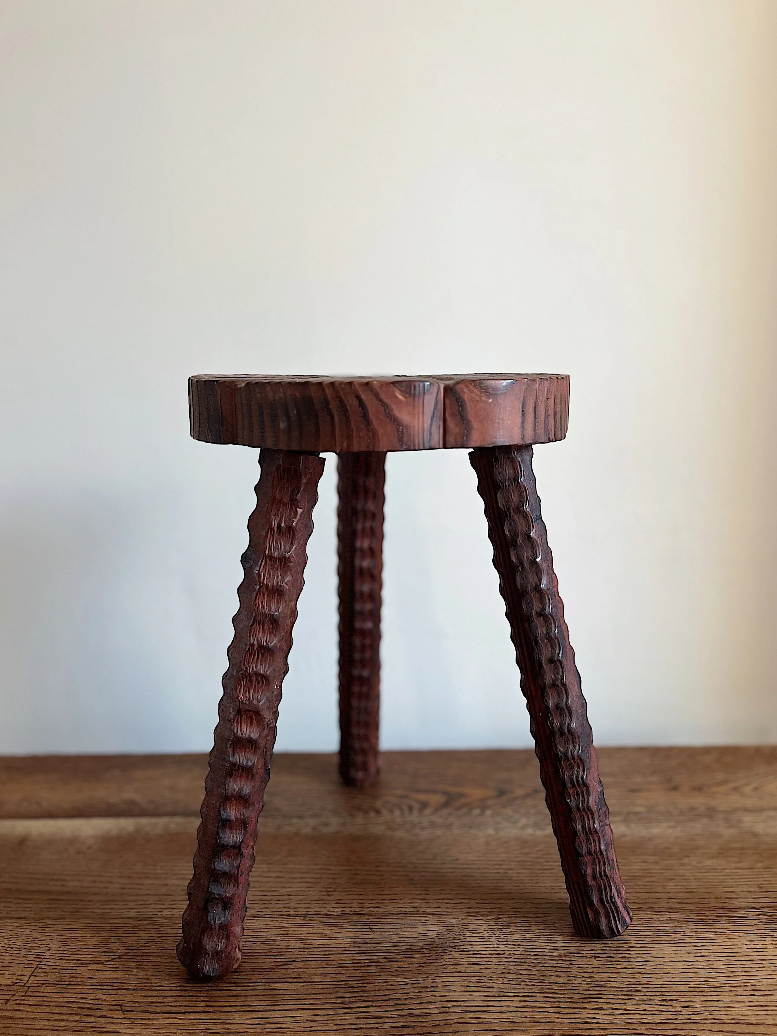 Wooden stool with a round seat and textured legs on a wooden surface.