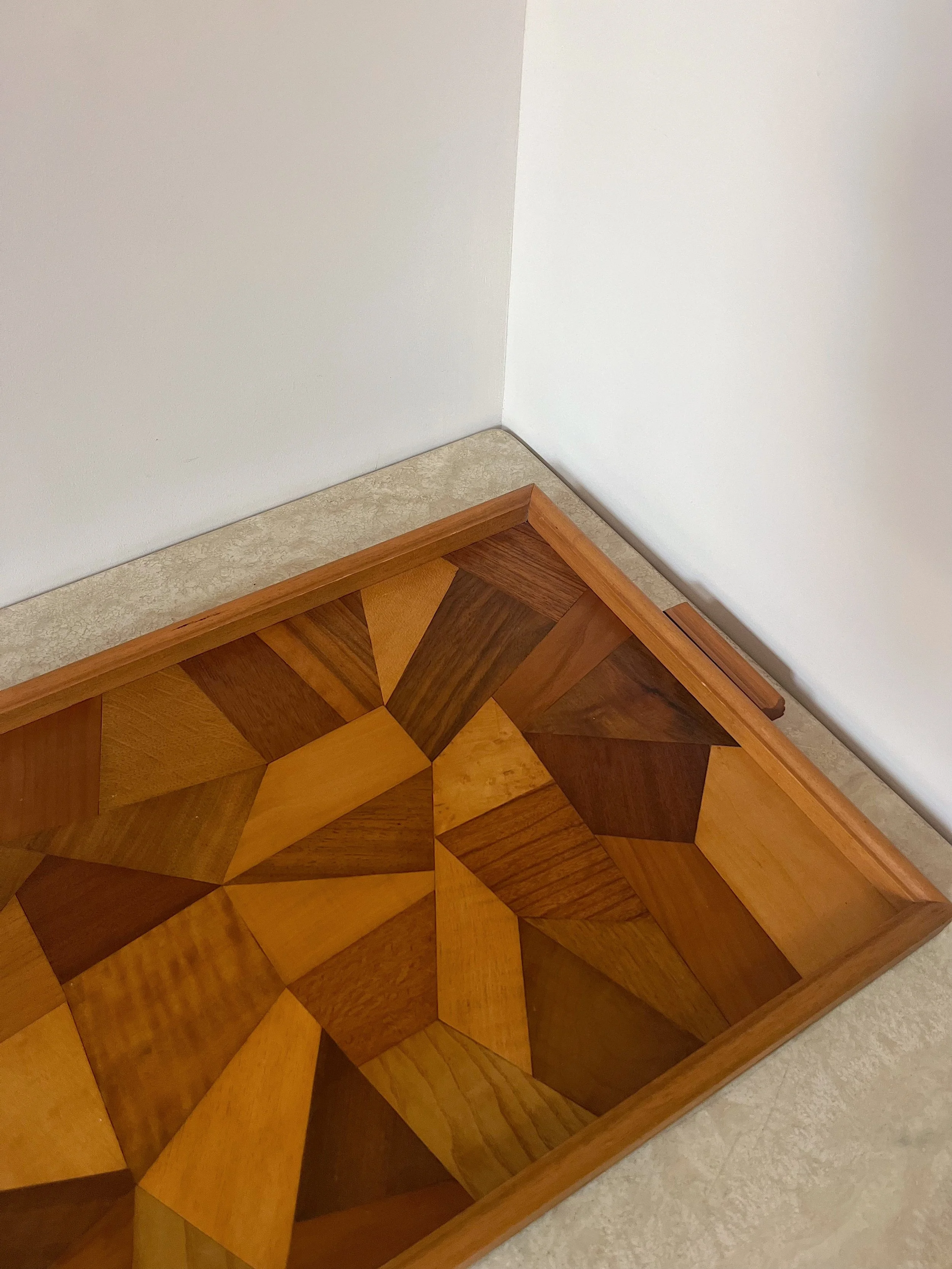 Geometric wooden tray with various shades of wood on a light-colored surface, against a white wall corner.