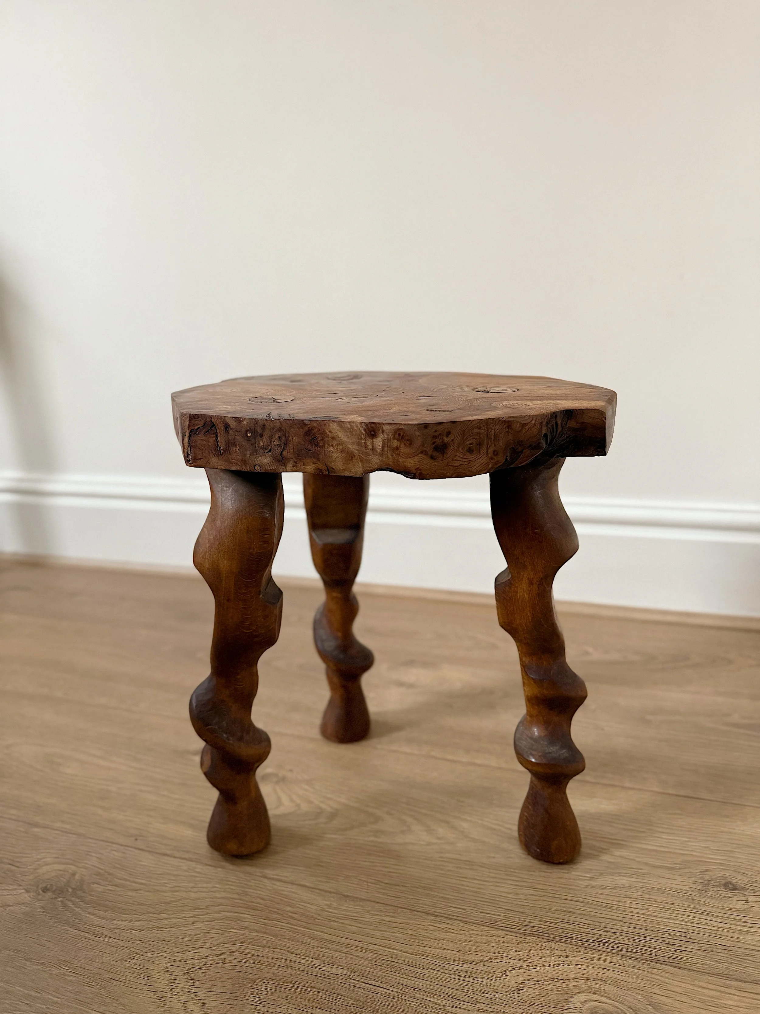 A small wooden stool with intricately carved legs and a rustic design on a wooden floor.