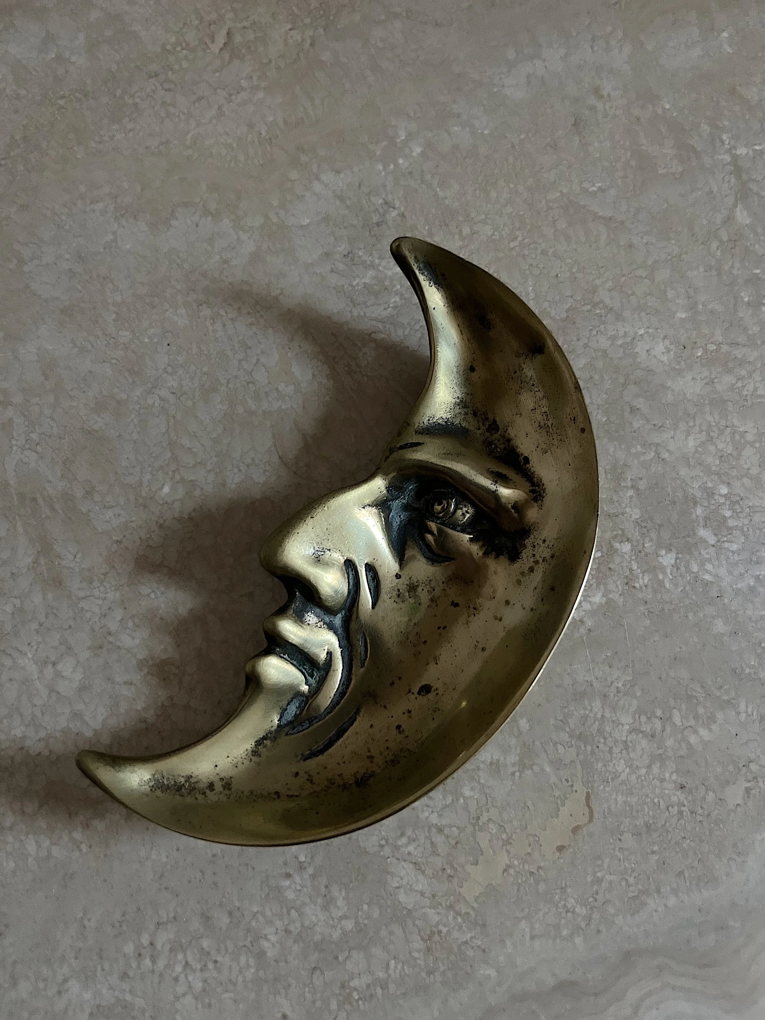 Metallic crescent moon sculpture with a face