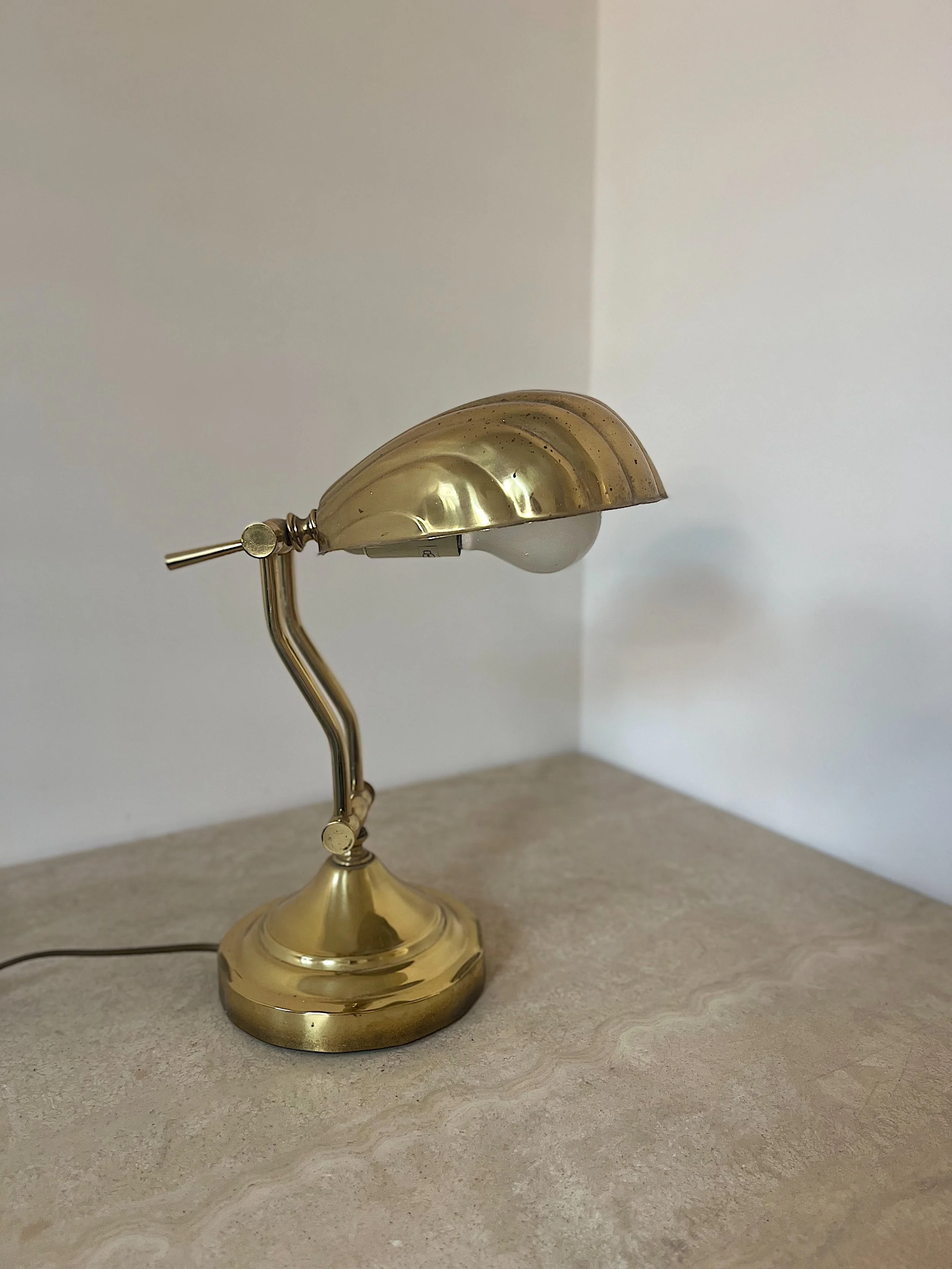 Vintage brass desk lamp on a stone surface with a curved design and dome-shaped shade.
