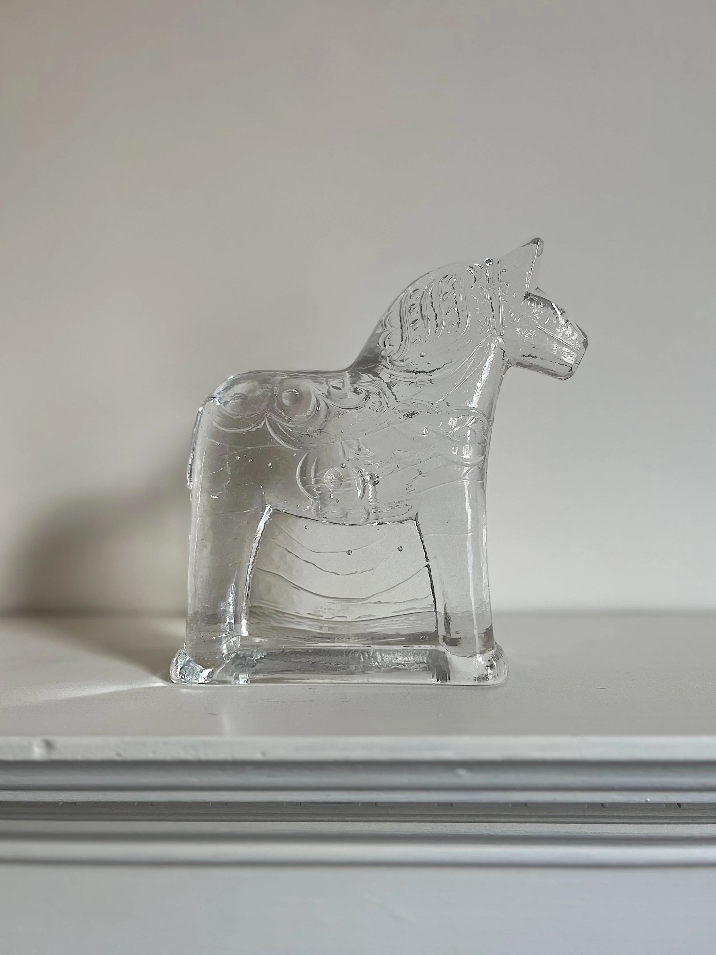 A clear glass figurine shaped like a horse on a white surface.
