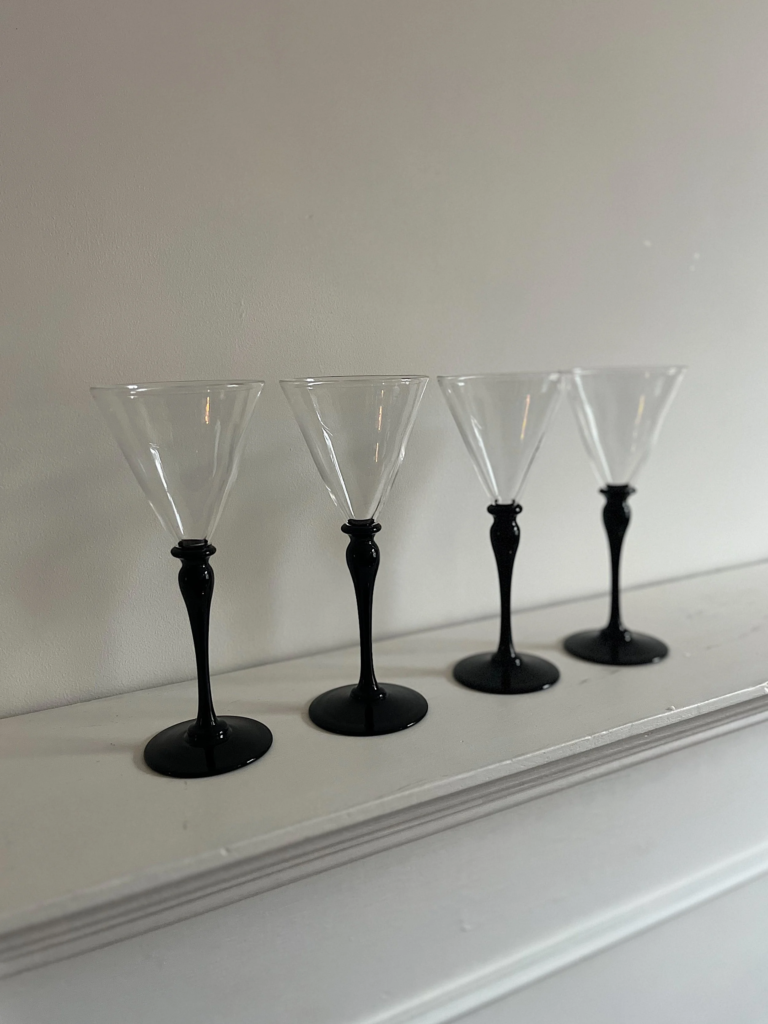 Four black-stemmed martini glasses on a white shelf.