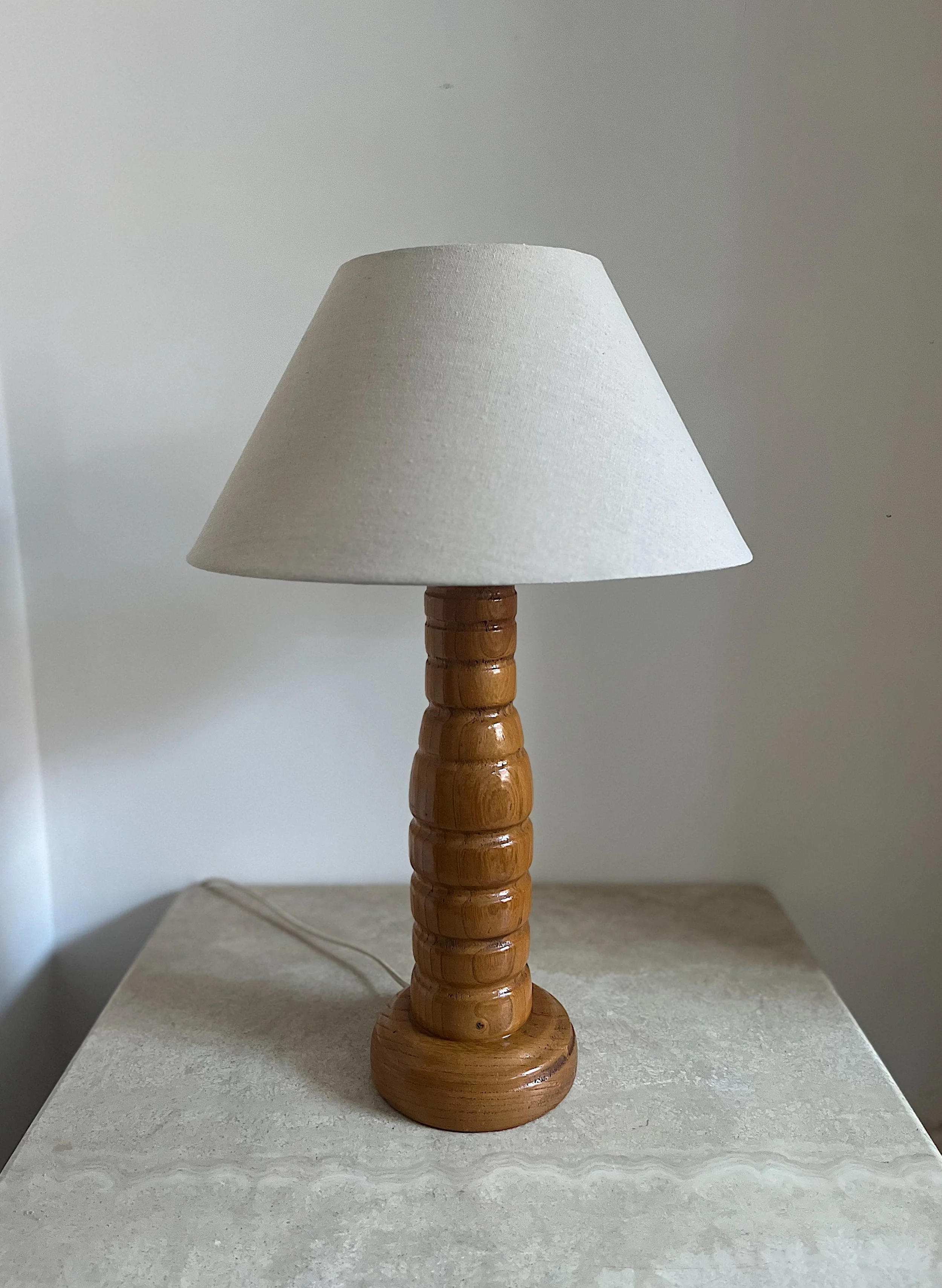 A table lamp with a wooden base and a white fabric lampshade on a light-colored surface.