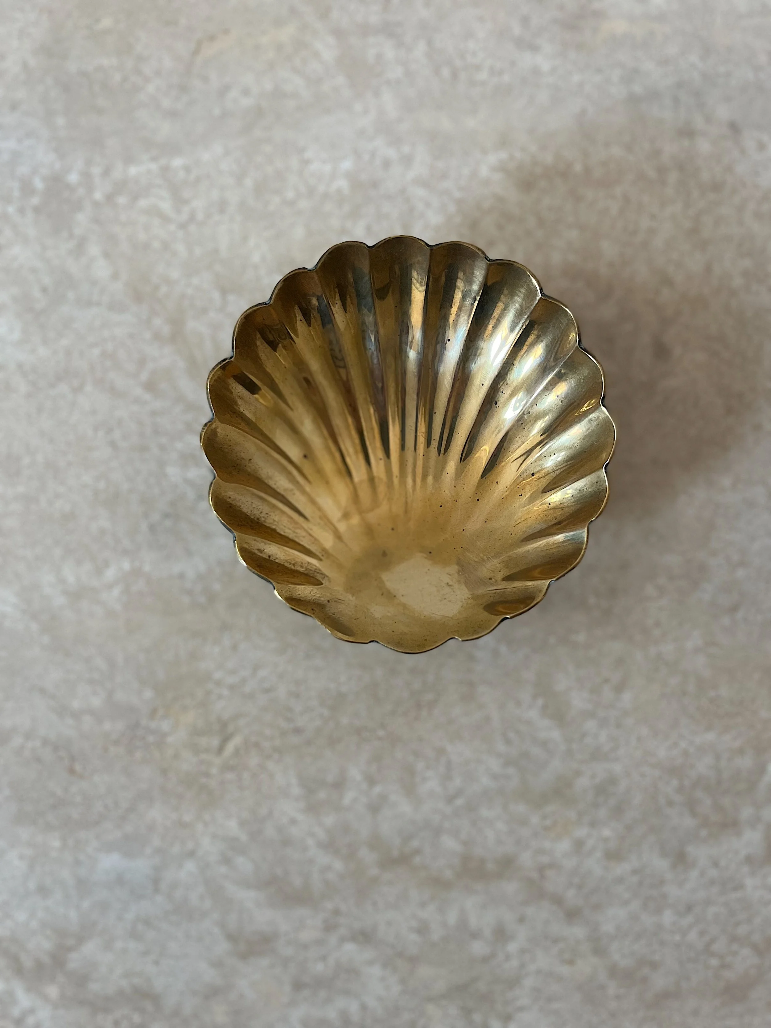 Top view of a brass fluted bowl on a light textured background.