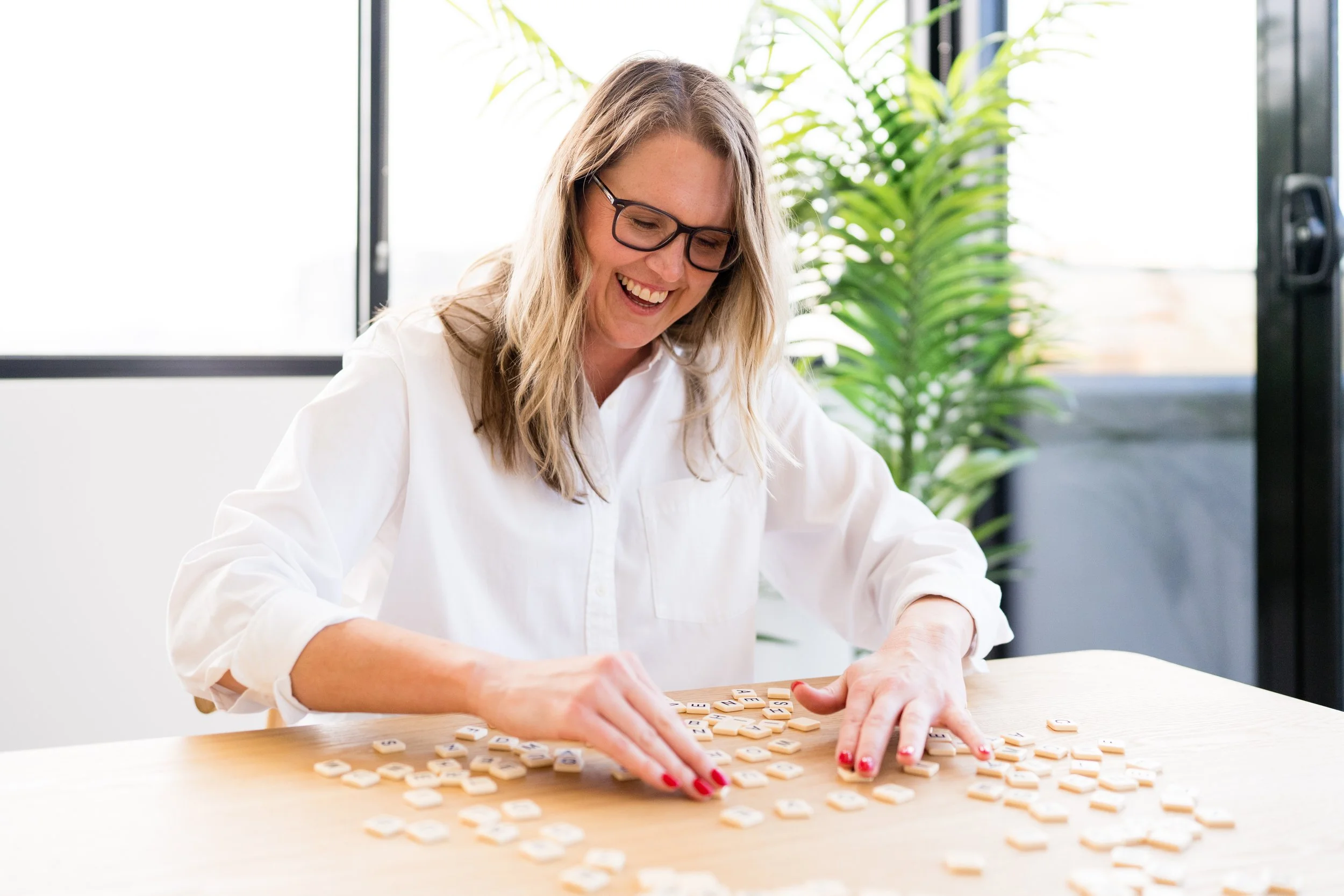 Kathy Rast smiles as she sifts through scattered letter tiles that are spread out across a wooden table.