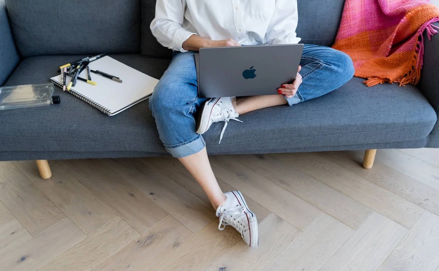 Kathy Rast sits with crossed legs on a grey sofa with her laptop resting on her lap