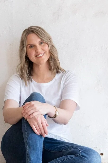 Kathy Rast smiles as sits on the floor while leaning against a white wall.jpg