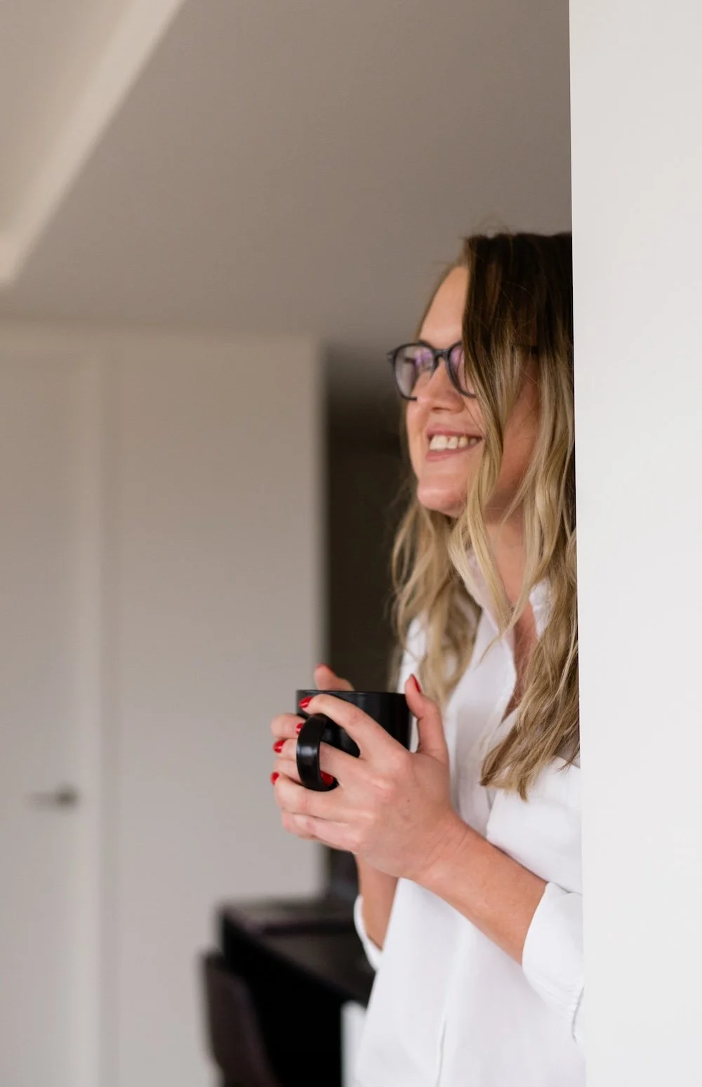 Kathy Rast leans against a wall while holding a mug between both of her hands