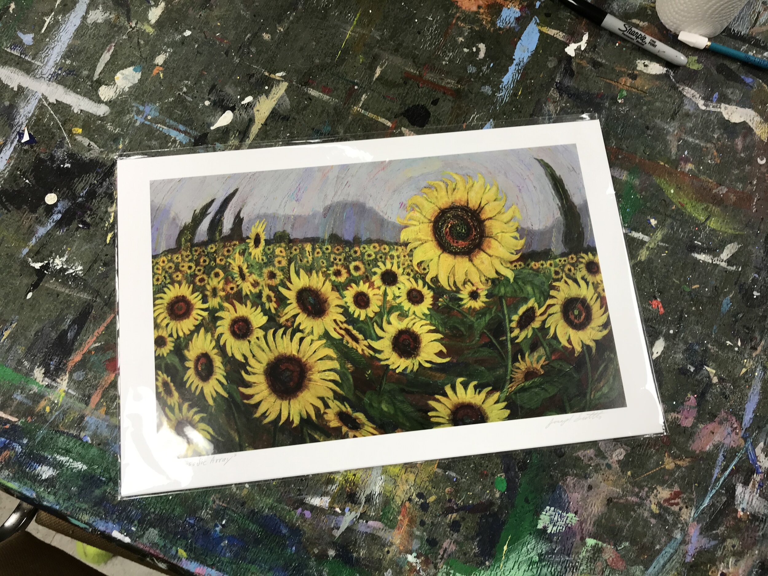 This is an original painting by Joseph Suttle of a field of sunflowers with distant trees and mountains painted over a colorful spiral of paint.