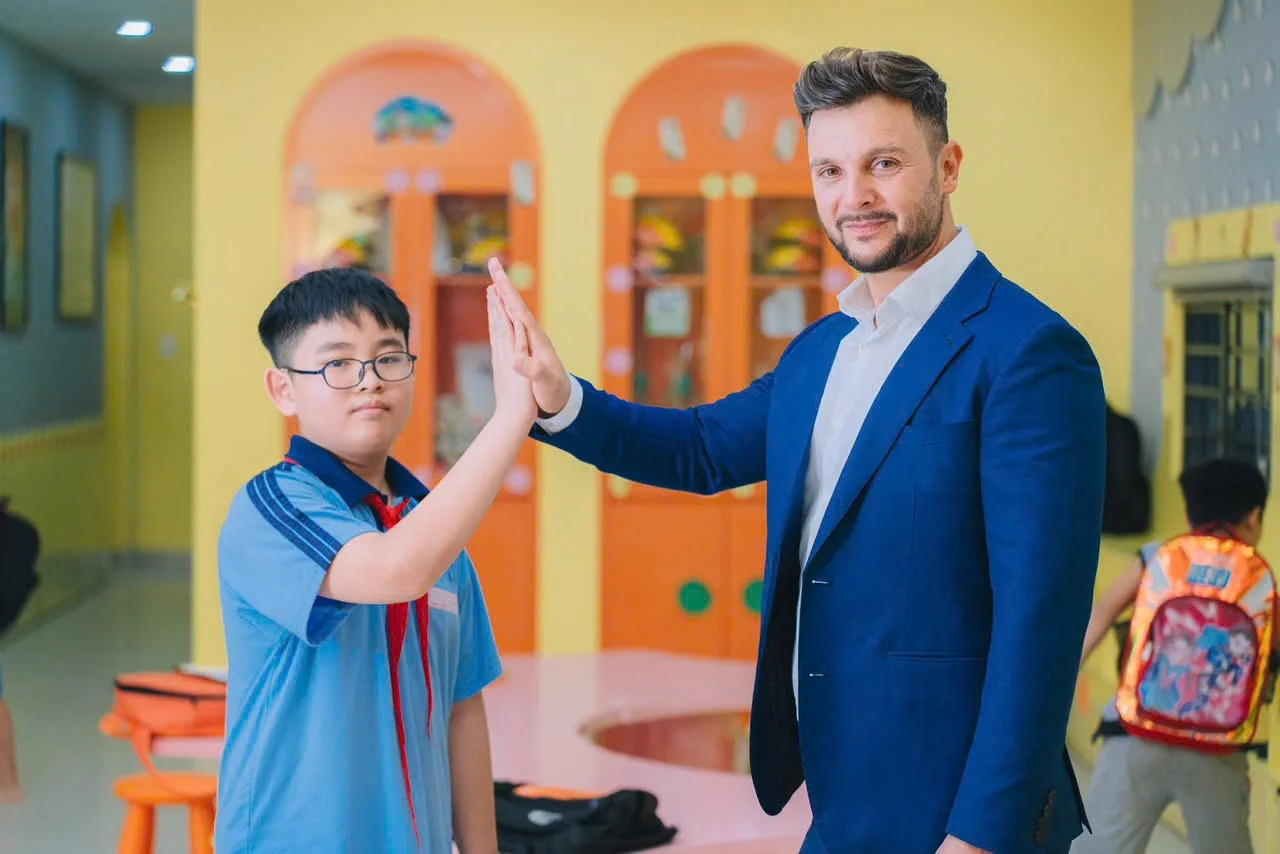 A schoolboy giving a high-five to a man in a blue blazer inside a classroom.