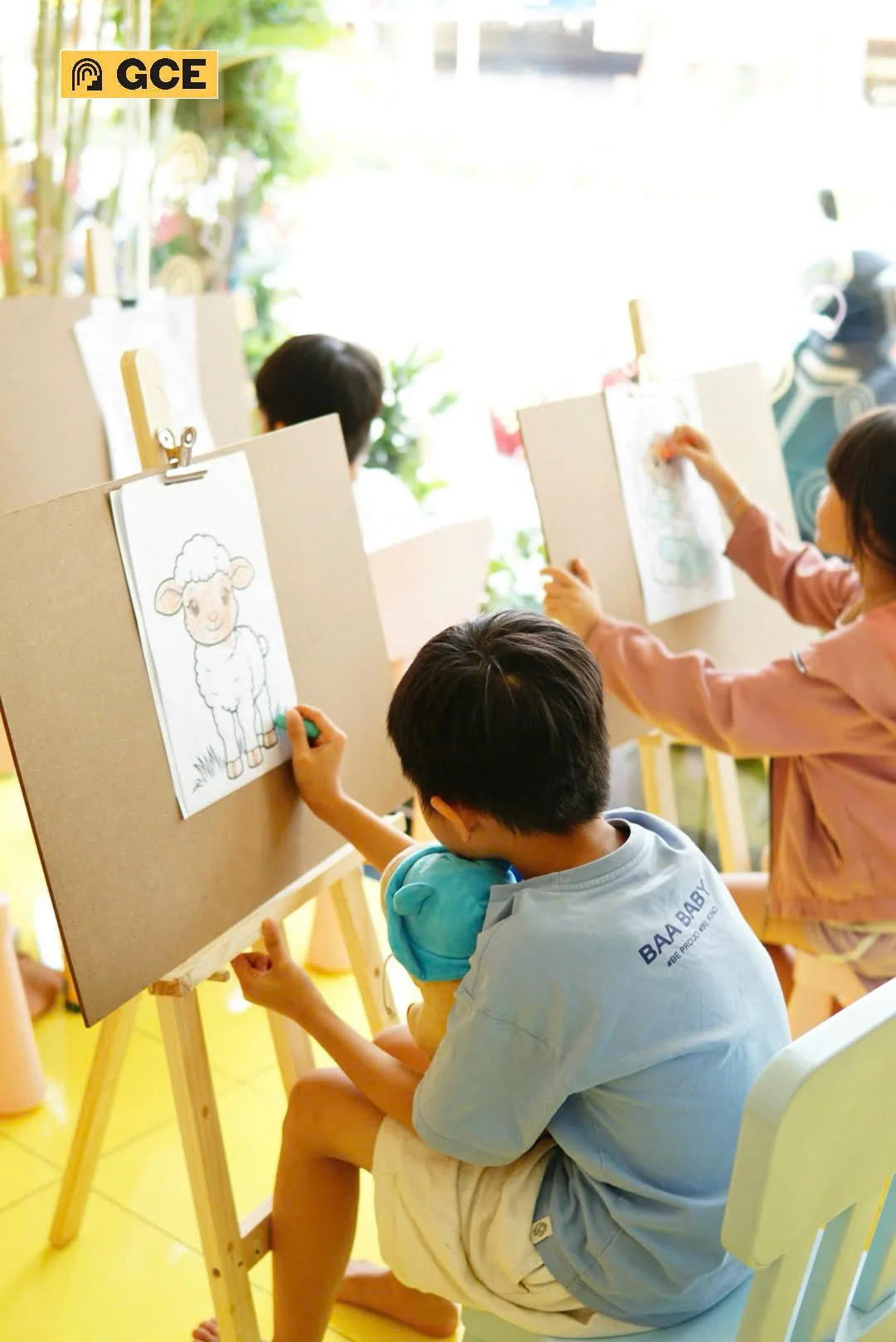 Children coloring pictures of farm animals on drawing boards in a brightly lit room.