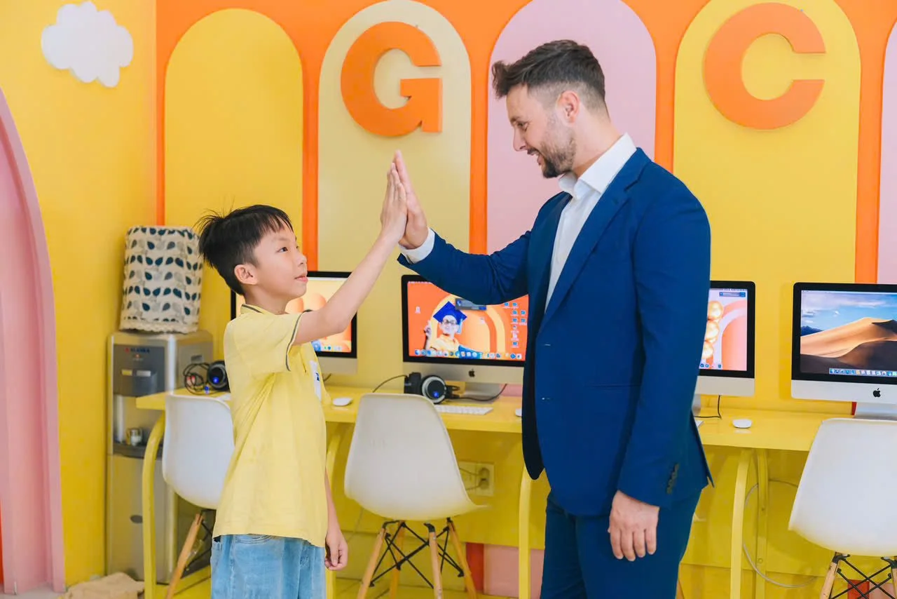 A young boy and an adult man giving each other a high five in a colorful room with computers and large letter decorations on the wall.