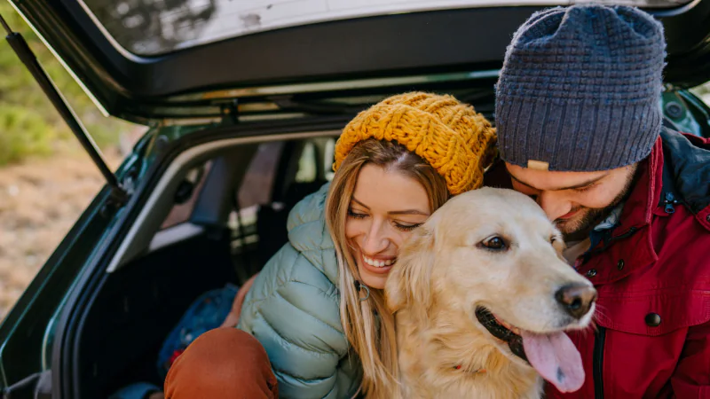 Happy couple with a dog getting out of a car in an outdoor setting