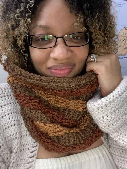 Nadine Johnson of BuddyLuvsCrochet in glasses and a brown striped crochet cowl