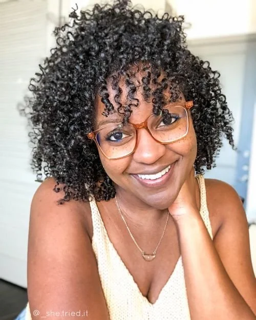 Carita Stewart of She Tried It! smiling in amber glasses and a cream knit top