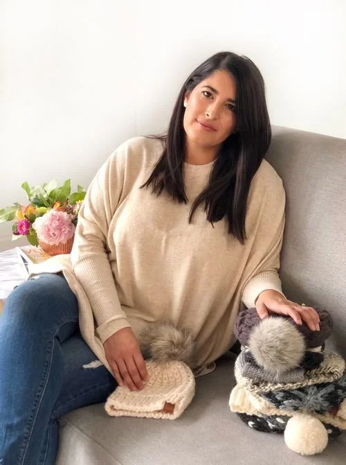 Candice Le of URBN FIBER on a sofa in a cream sweater, surrounded by knit beanies