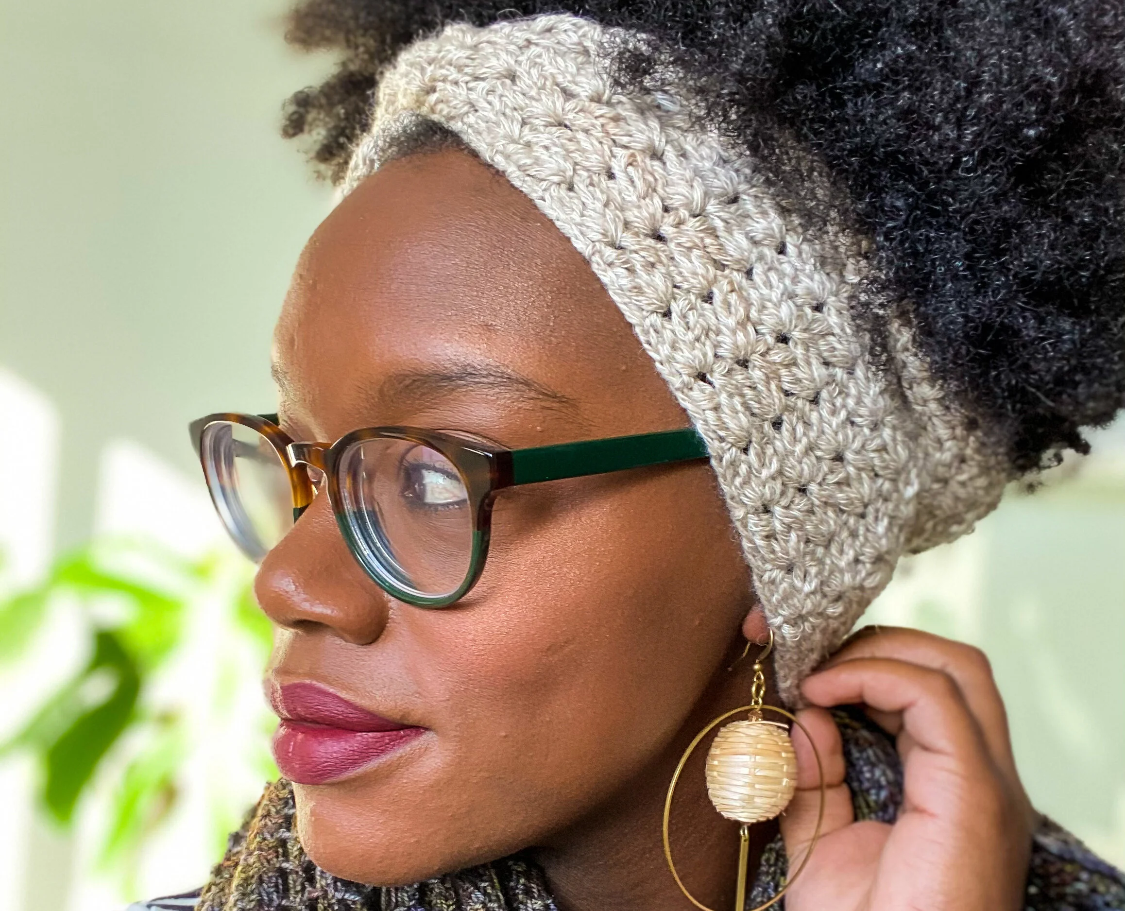 Side view of a woman in glasses wearing the Cara Earwarmer, a textured oatmeal crochet earwarmer. Free beginner crochet pattern.