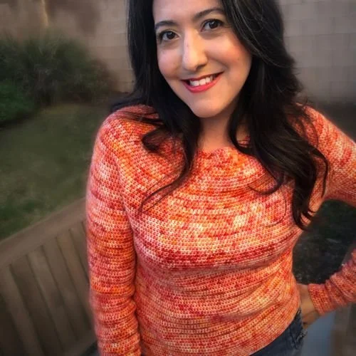 Rebecca Mercado of Filum Revelo smiling in a speckled orange and red crochet sweater