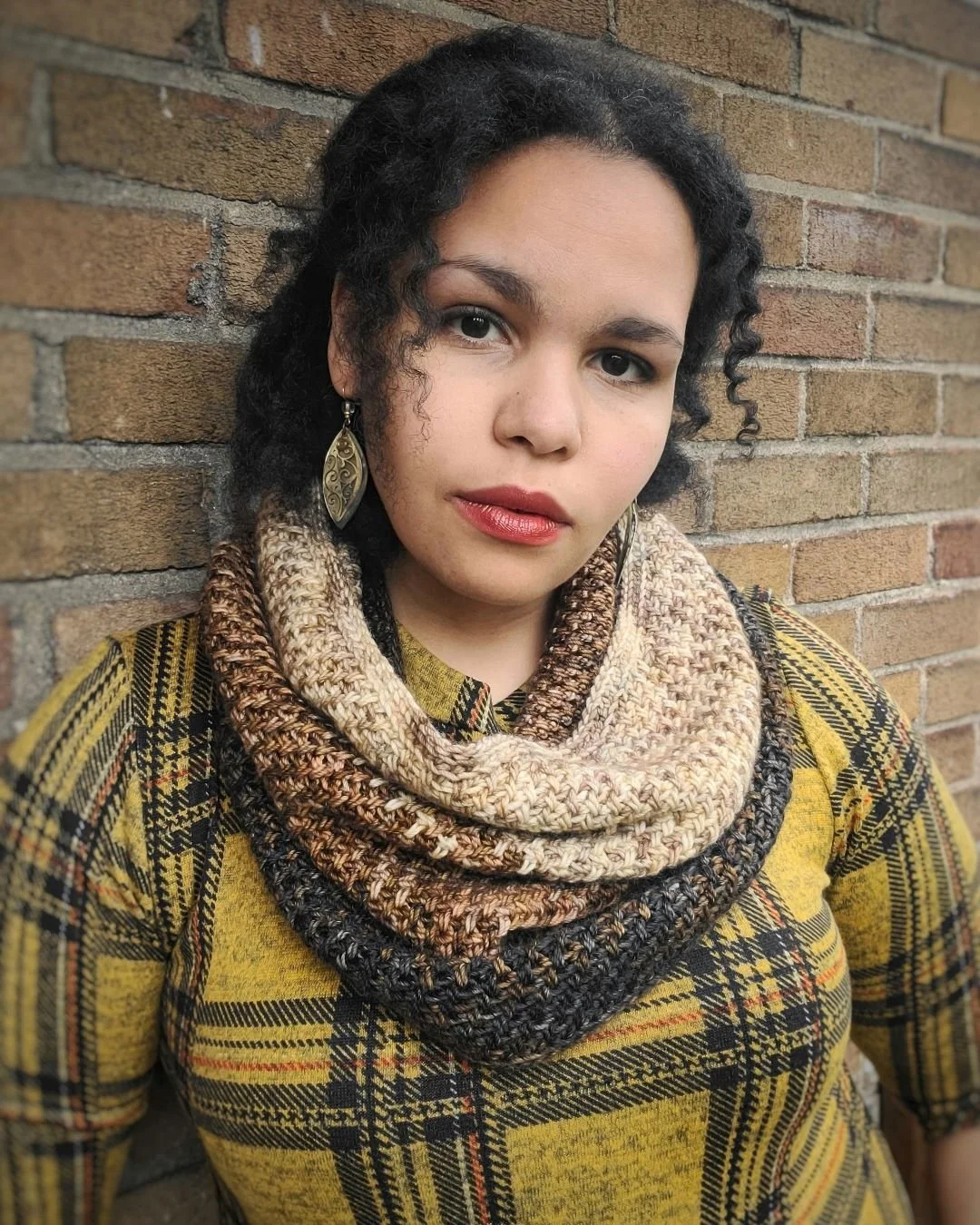 Person wearing a plaid yellow and black top and a multicolored knitted scarf.