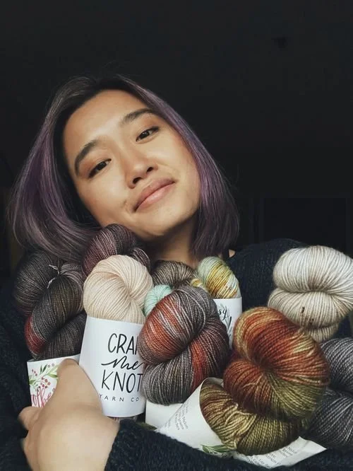 Angela Wong of AW Knits smiling while holding an armful of hand-dyed yarn skeins